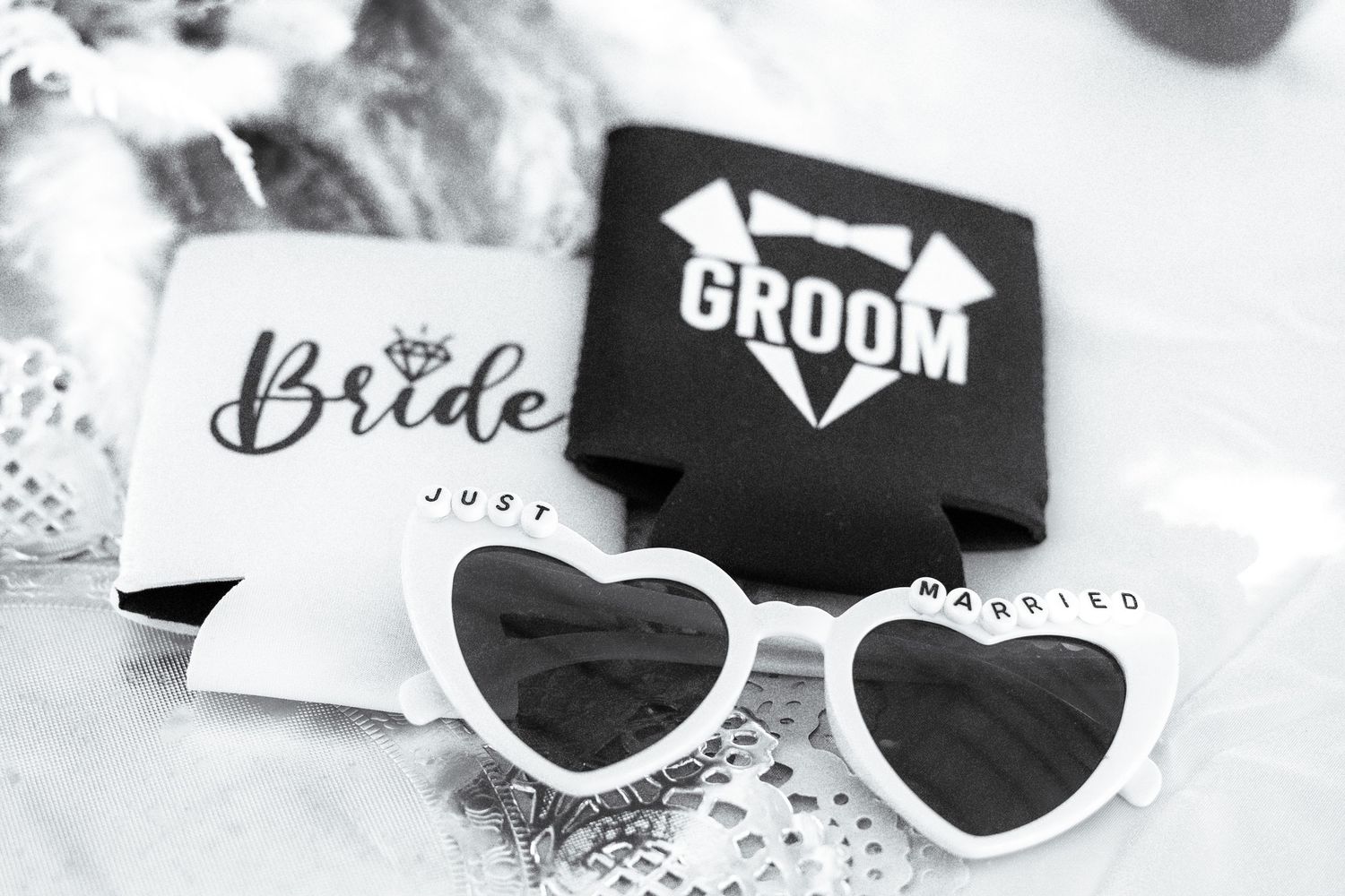 White sunglasses decorated with bride and groom text lay on a white surface with sparkly wedding decorations.
