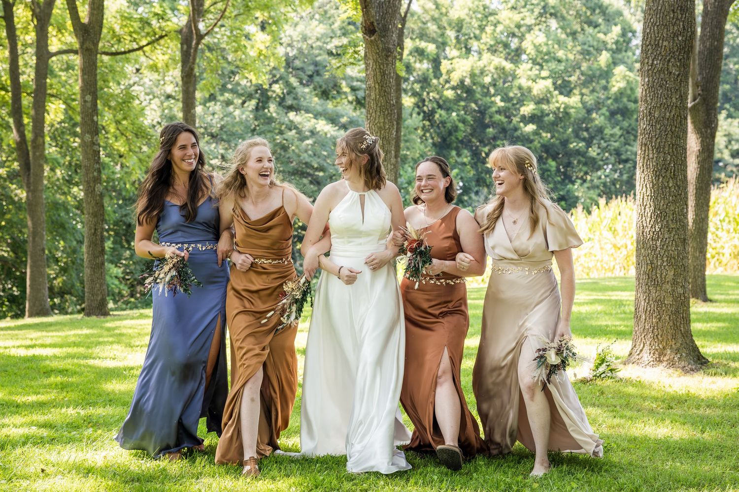 A group in formal attire sits together on grass under shady trees during an outdoor gathering.