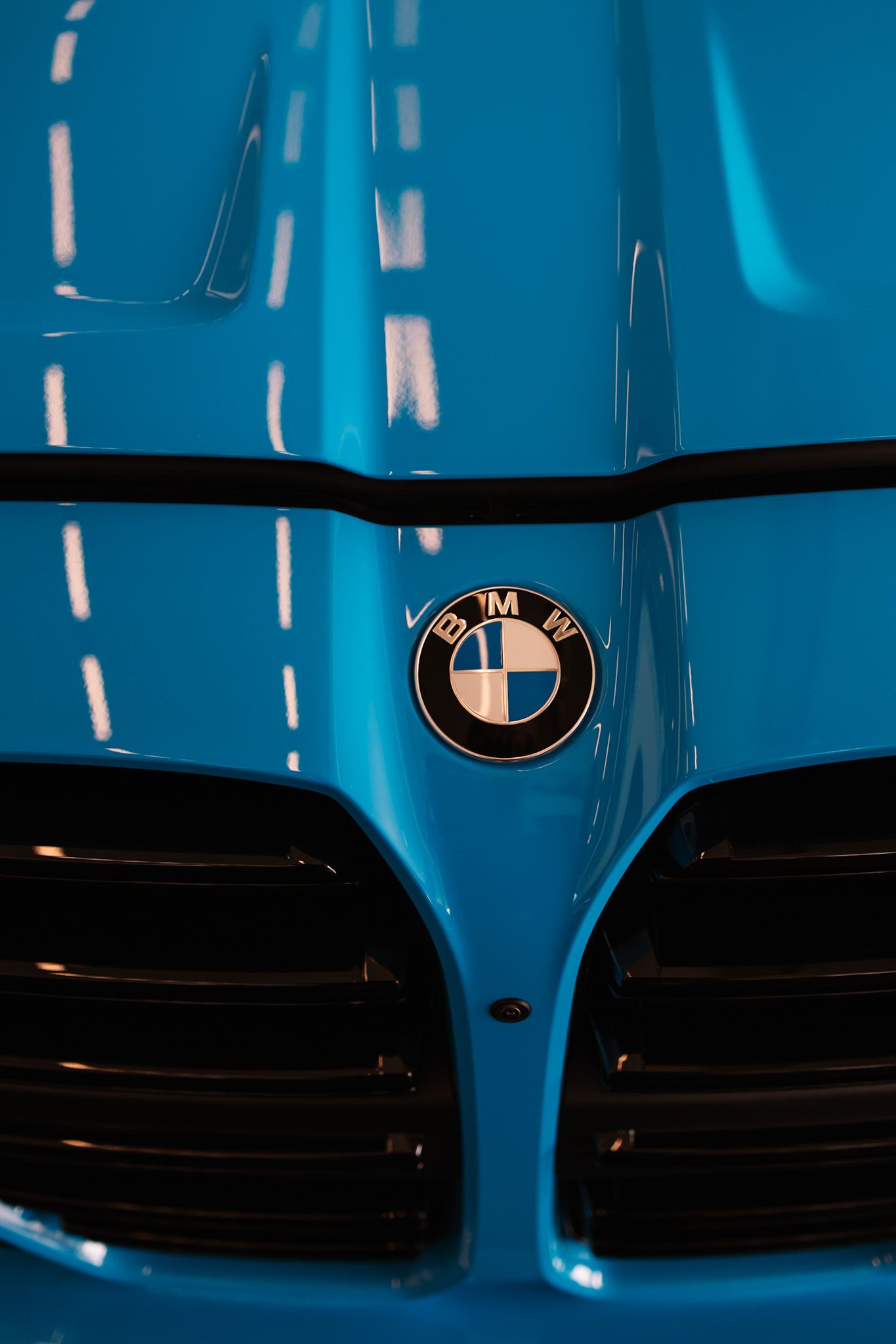 Close-up of a glossy blue BMW car hood featuring the iconic BMW roundel logo above the black kidney grille.