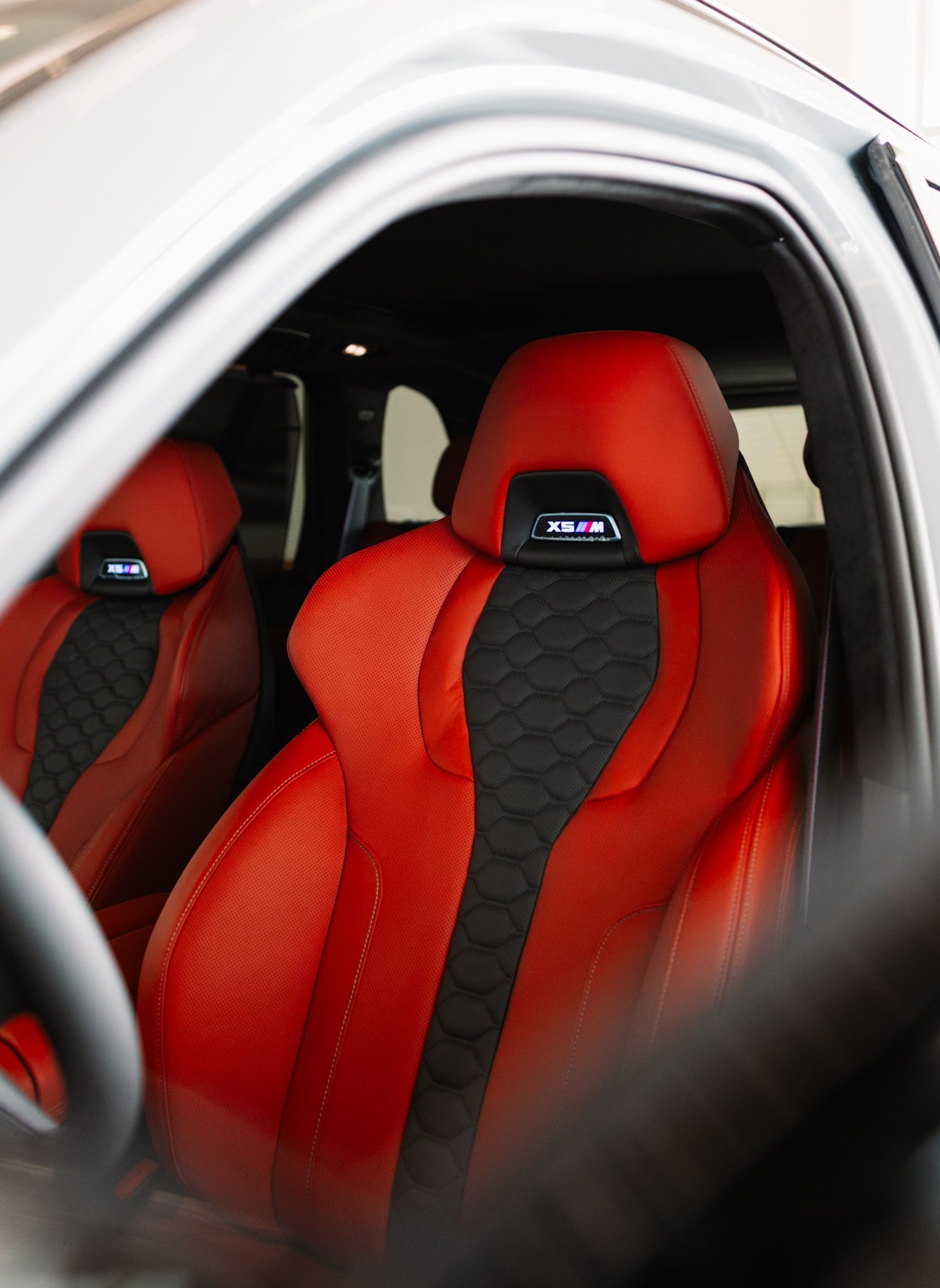 Luxury BMW X5 M red and black quilted leather sport seats with embroidered headrest logos.