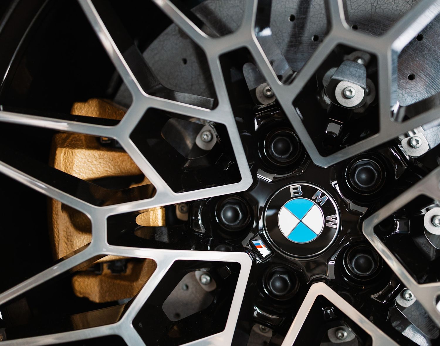 Close-up of a BMW alloy wheel featuring the iconic BMW logo center cap with gold brake calipers visible behind.