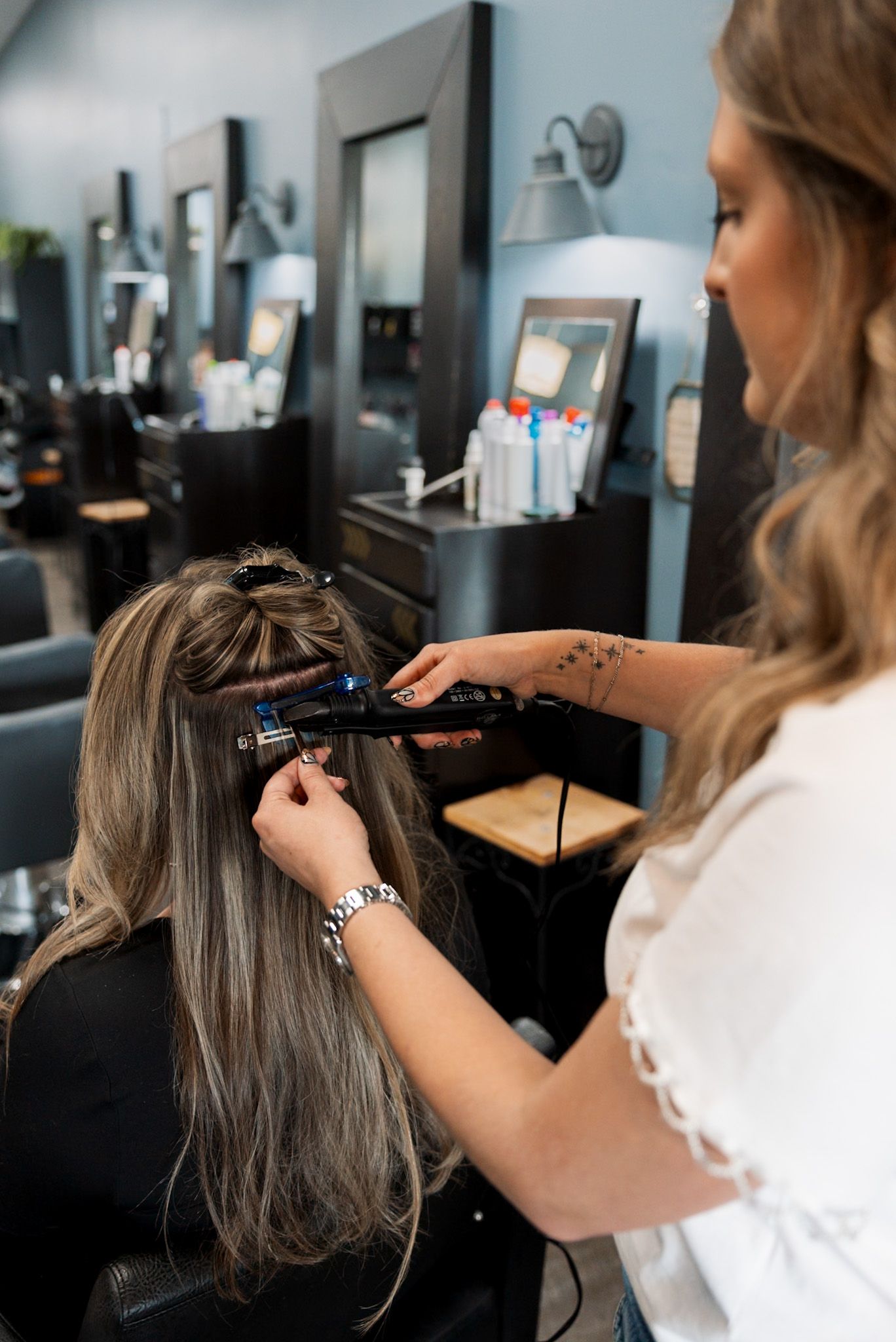 Hair stylist using a curling iron on a client's long blonde hair in a modern salon.