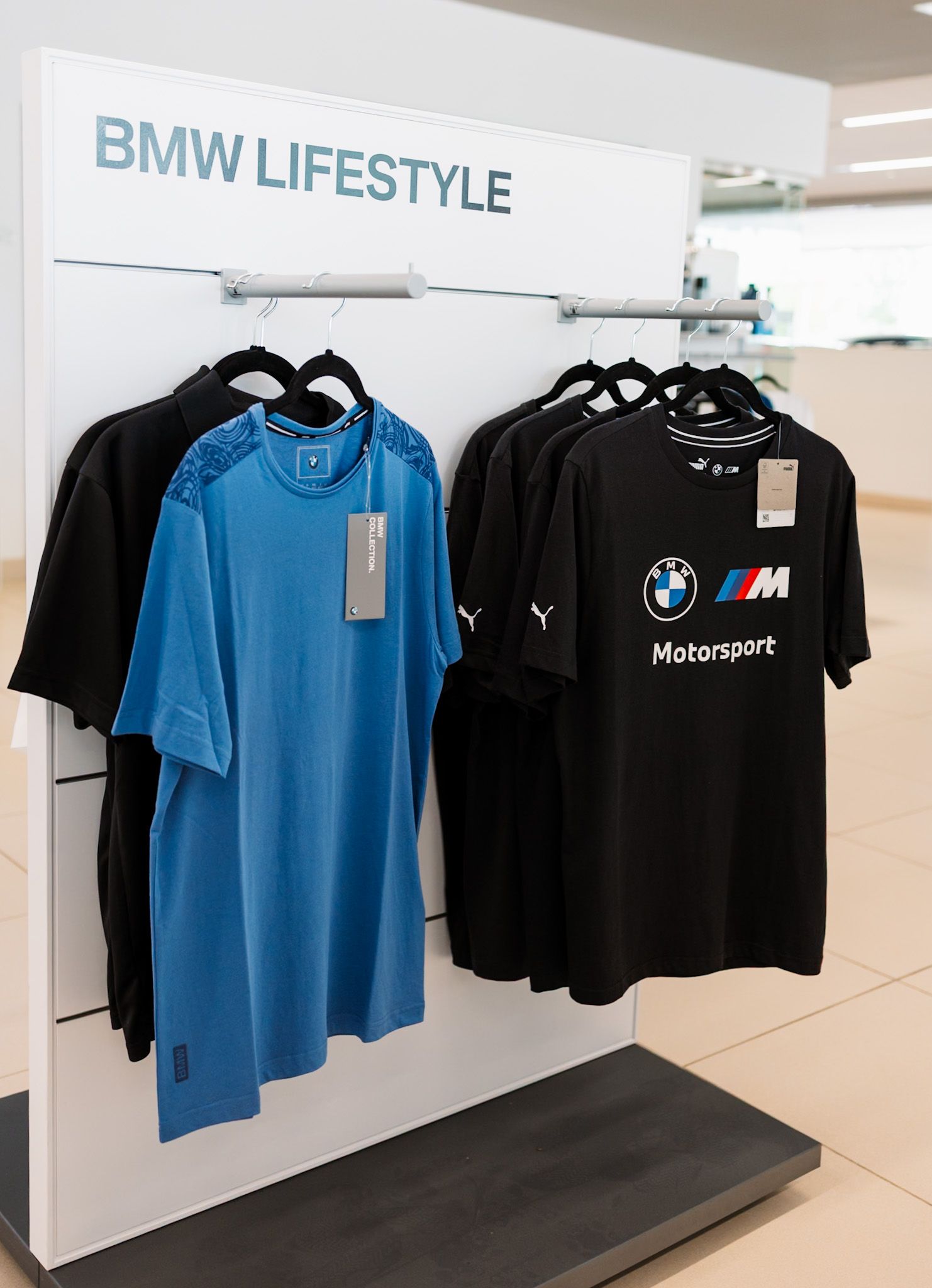 BMW Lifestyle store display featuring Puma BMW M Motorsport black and blue t-shirts hanging on a white retail fixture.