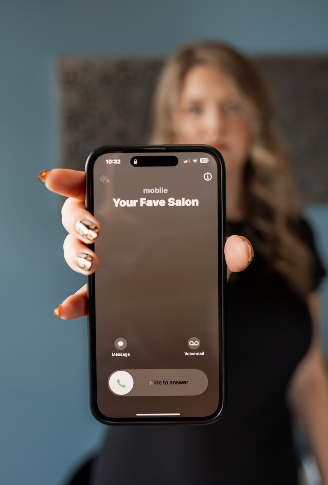 Woman holding iPhone displaying incoming call from Your Fave Salon, showcasing nail art with gold accents.
