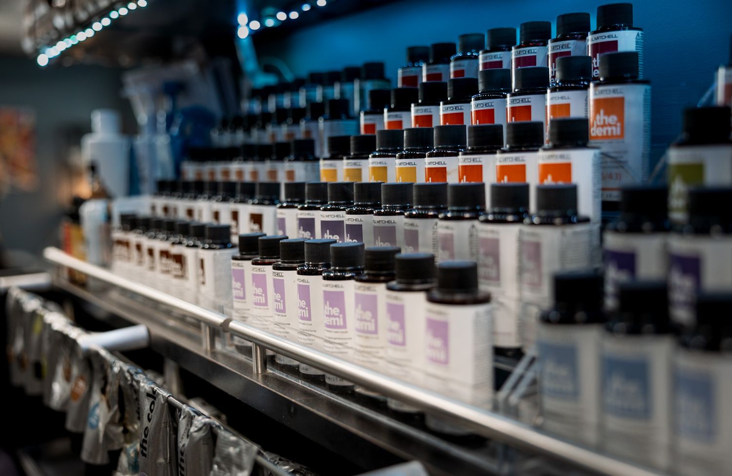 Rows of colorful hair dye bottles neatly arranged on metal shelves in a professional salon supply display.
