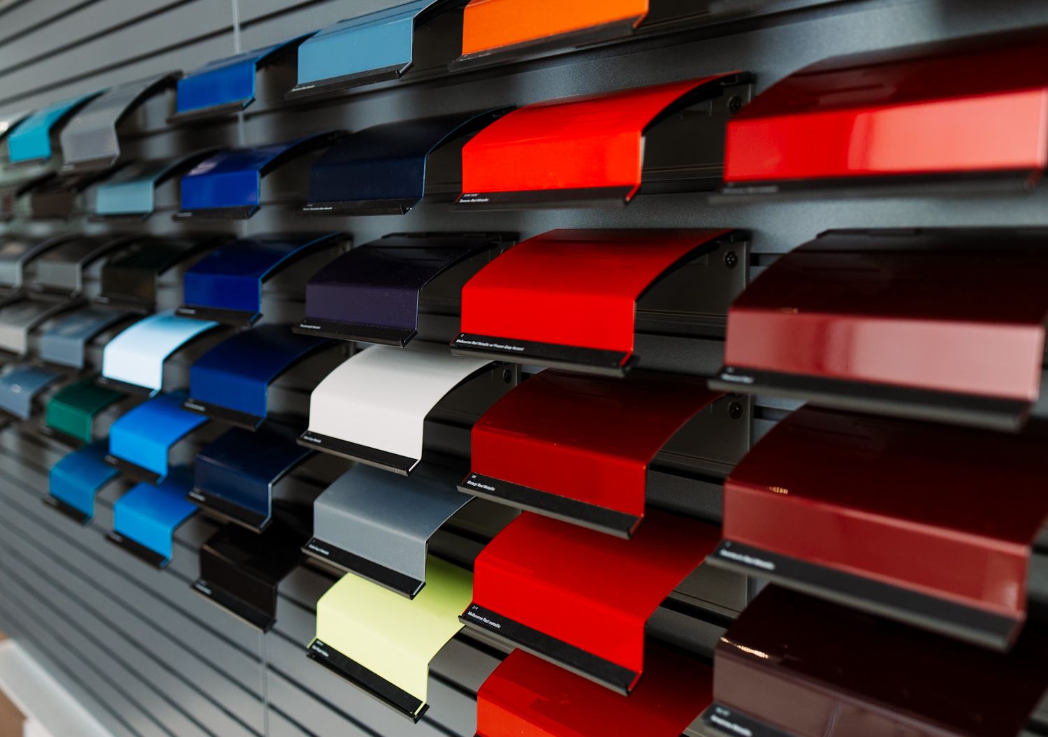 Colorful metal paint sample panels displayed on a wall rack, showcasing various automotive or industrial color options.
