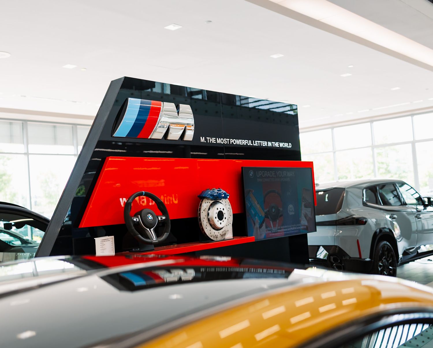 BMW M showroom display featuring iconic M logo, steering wheel, and brake disc exhibit in a luxury car dealership.