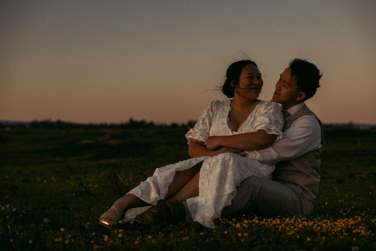 a cinematic filmy photo of a groom and bride laying together on a hillside in California as the sun sets behind them