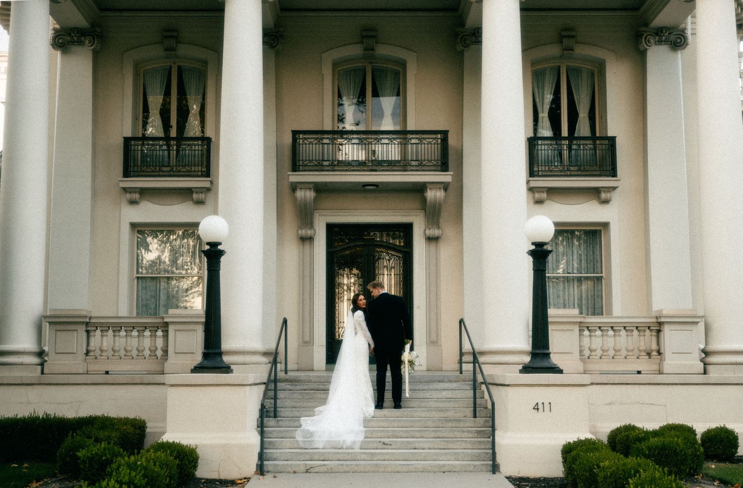 a cinematic filmy photo of a bride and groom walking up steps of an old fashioned venue in a timeless pose