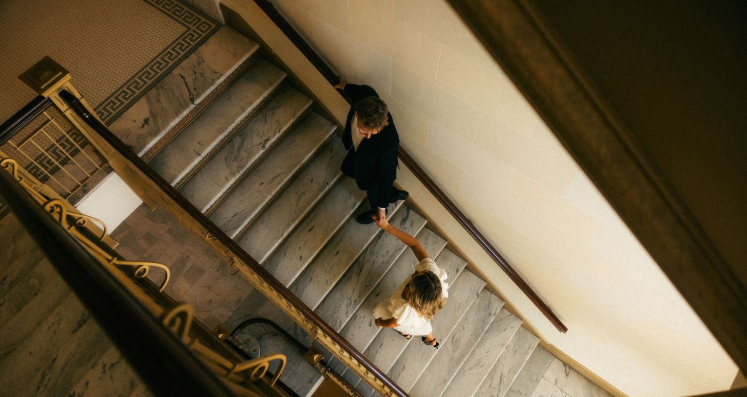a cinematic filmy photo of a groom leading his bride up the steps of the Utah capitol building