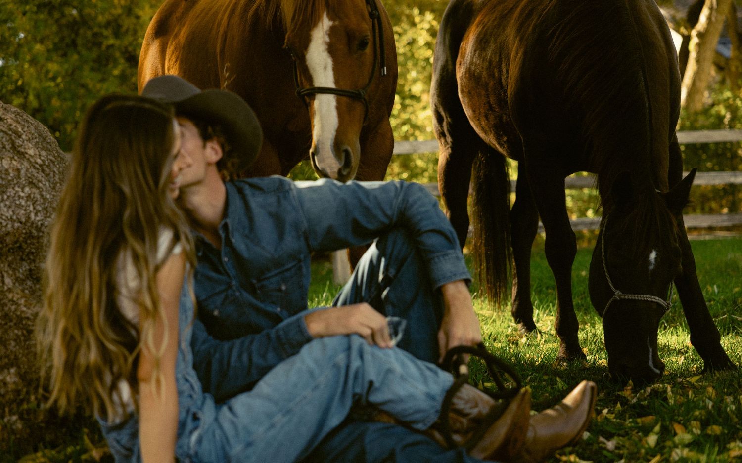 a documentary style photo of a kiss shared between lovers in the shade at a Utah ranch with horses on a fall day