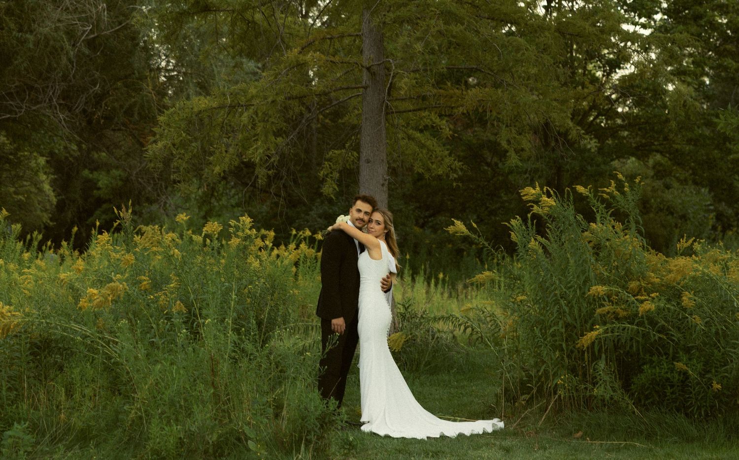 a cinematic filmy photo of a bride and groom hugging amongst wildflowers