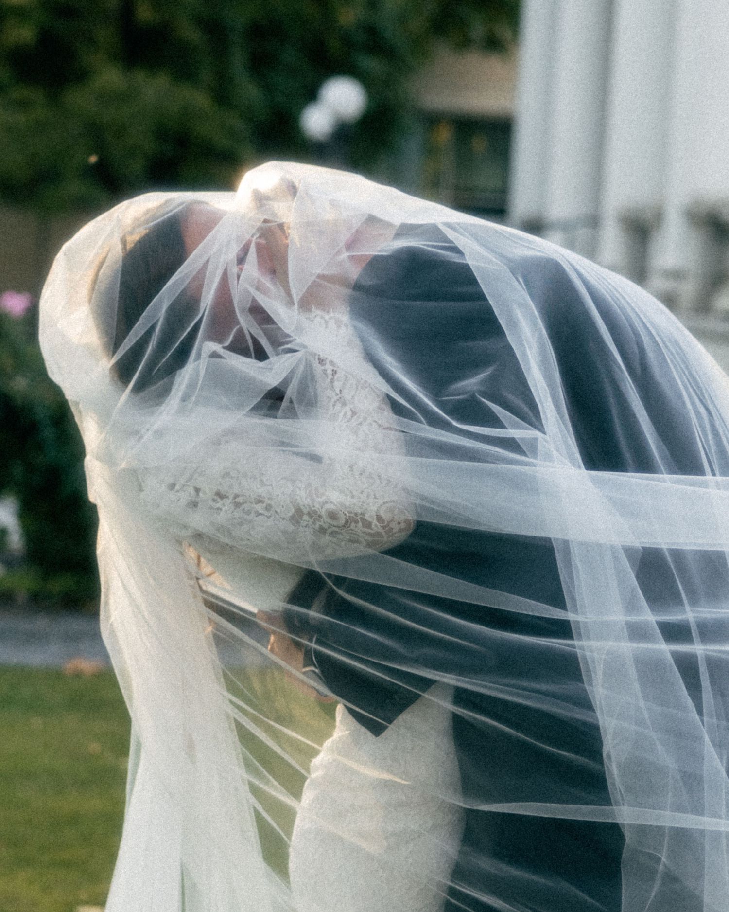 a cinematic filmy photo of a groom hugging his bride tightly under the veil with the sun highlighting the veil