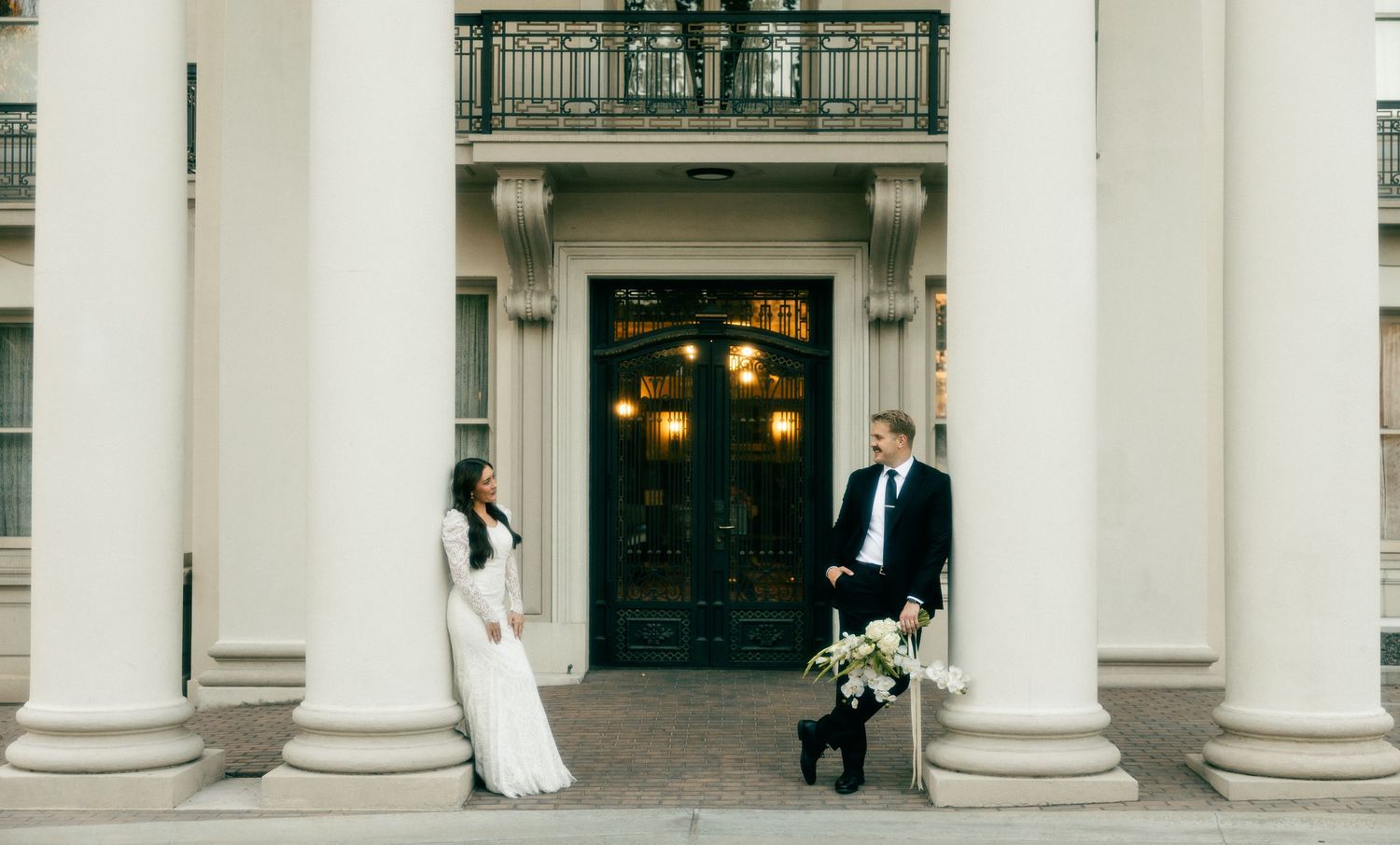 a cinematic filmy photo of a bride and groom looking at each other amongst columns of an old historical building