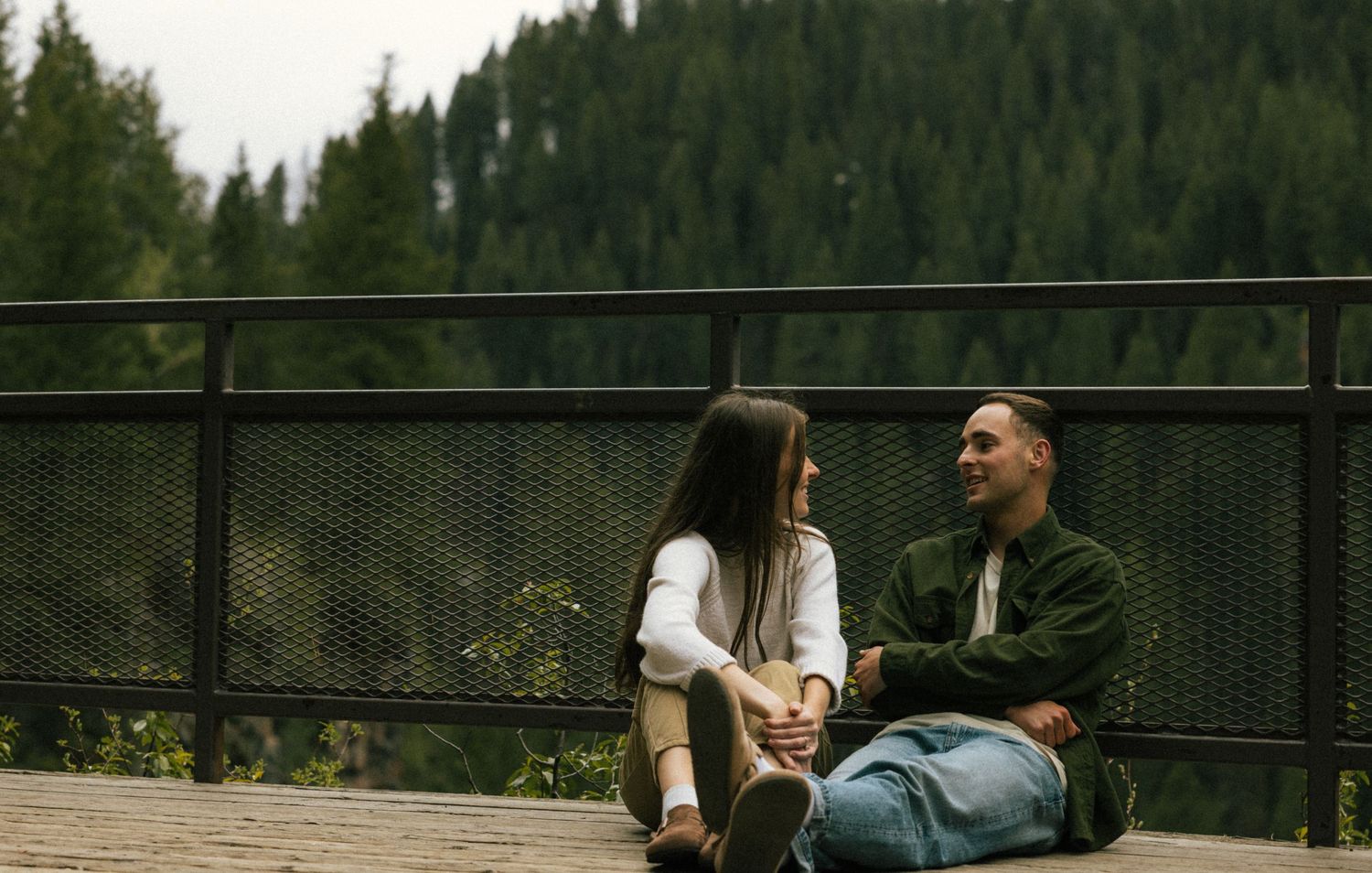 a cinematic filmy photo of a couple sharing a moment surrounded by green pine trees up near a waterfall