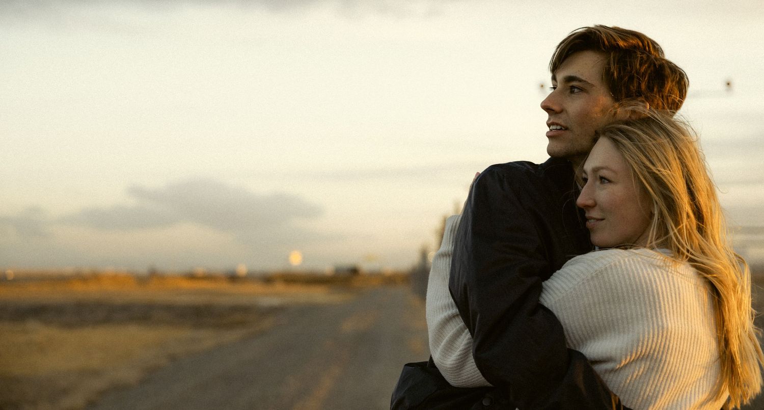 a cinematic film style photo of two lovers keeping each other warm as they watch the sun set on the mountains