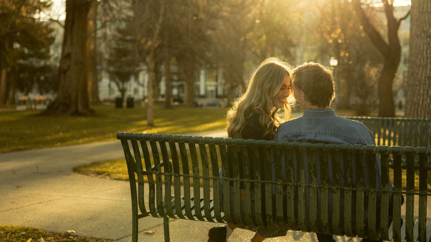 a cinematic filmy photo of a couple smiling together sitting on a park bench in the city as the sun shines on them