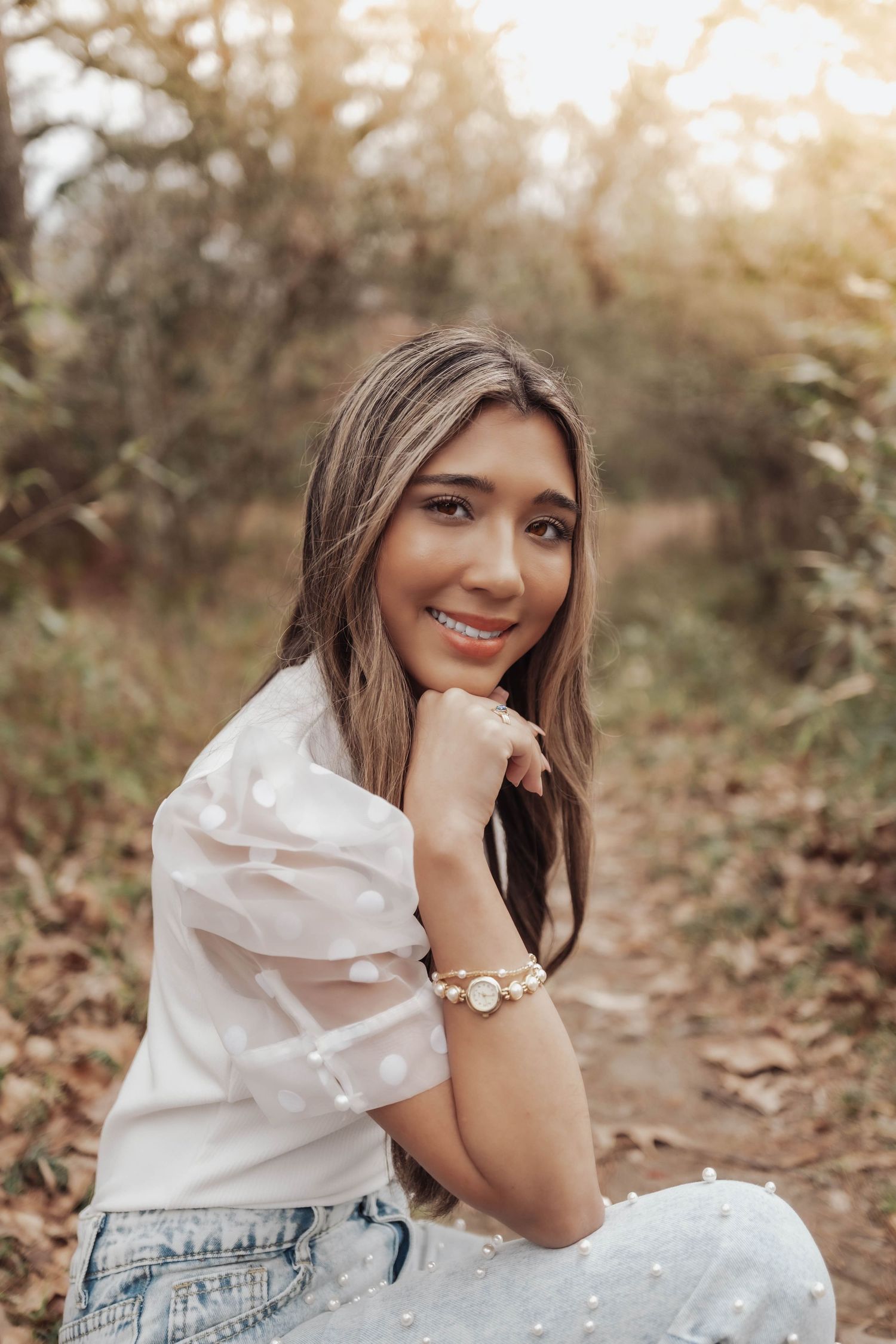A series of outdoor portrait photos showing someone in a white ruffled top and jeans sitting in autumn foliage at sunset.