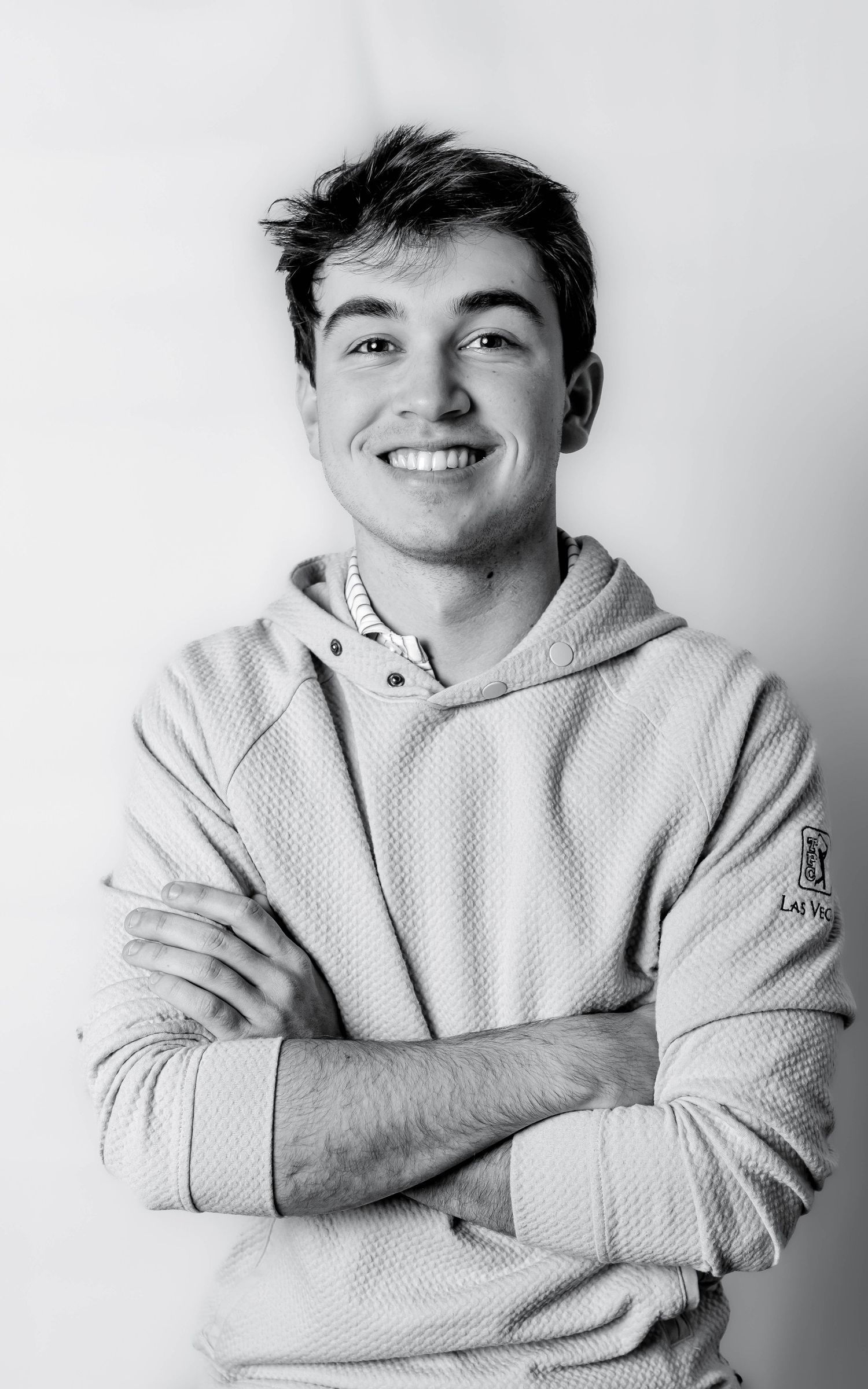 Smiling young man with crossed arms wearing a hoodie, black and white portrait photo.