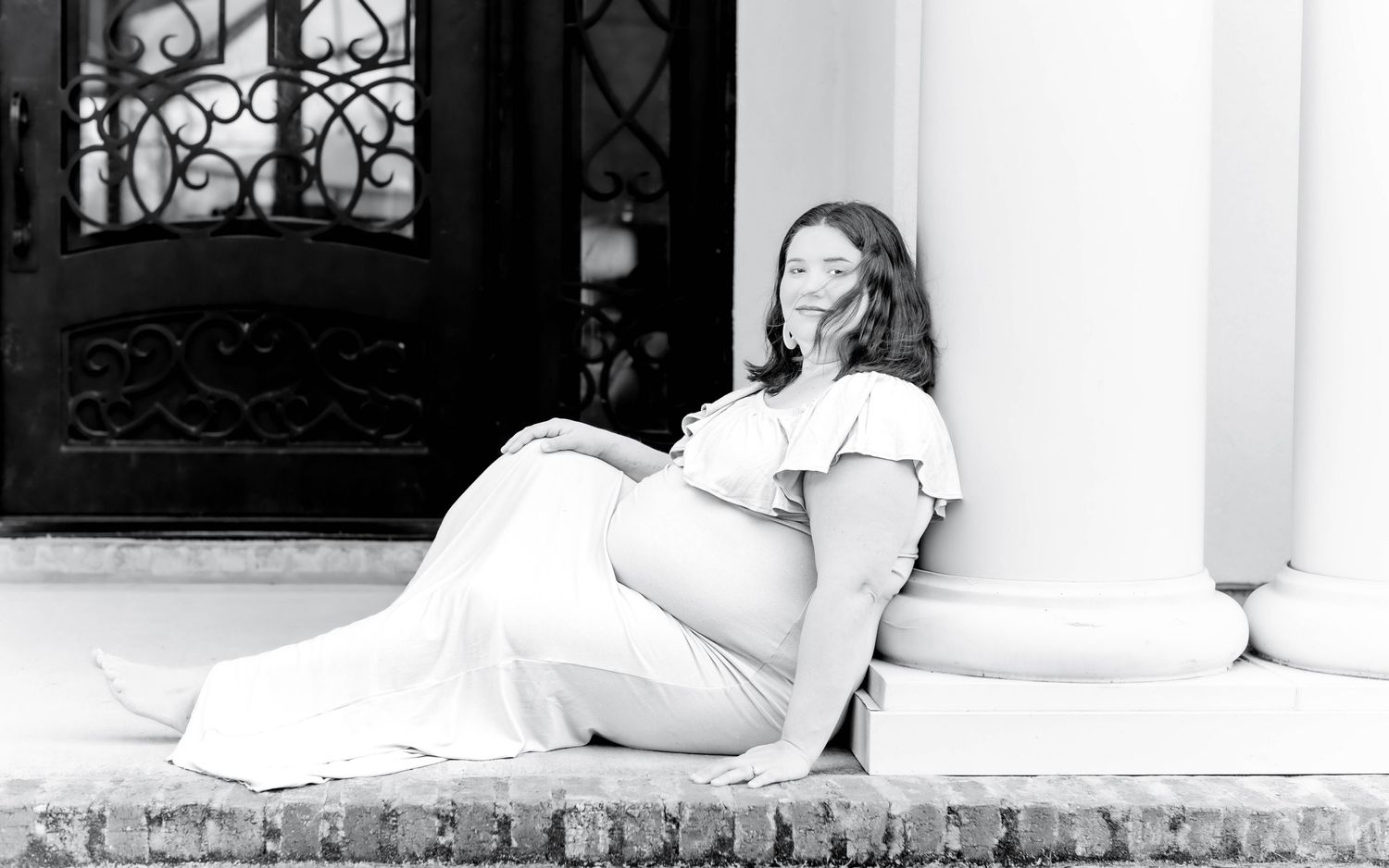 A black and white artistic photograph shows someone reclining against a pillar in a relaxed pose.