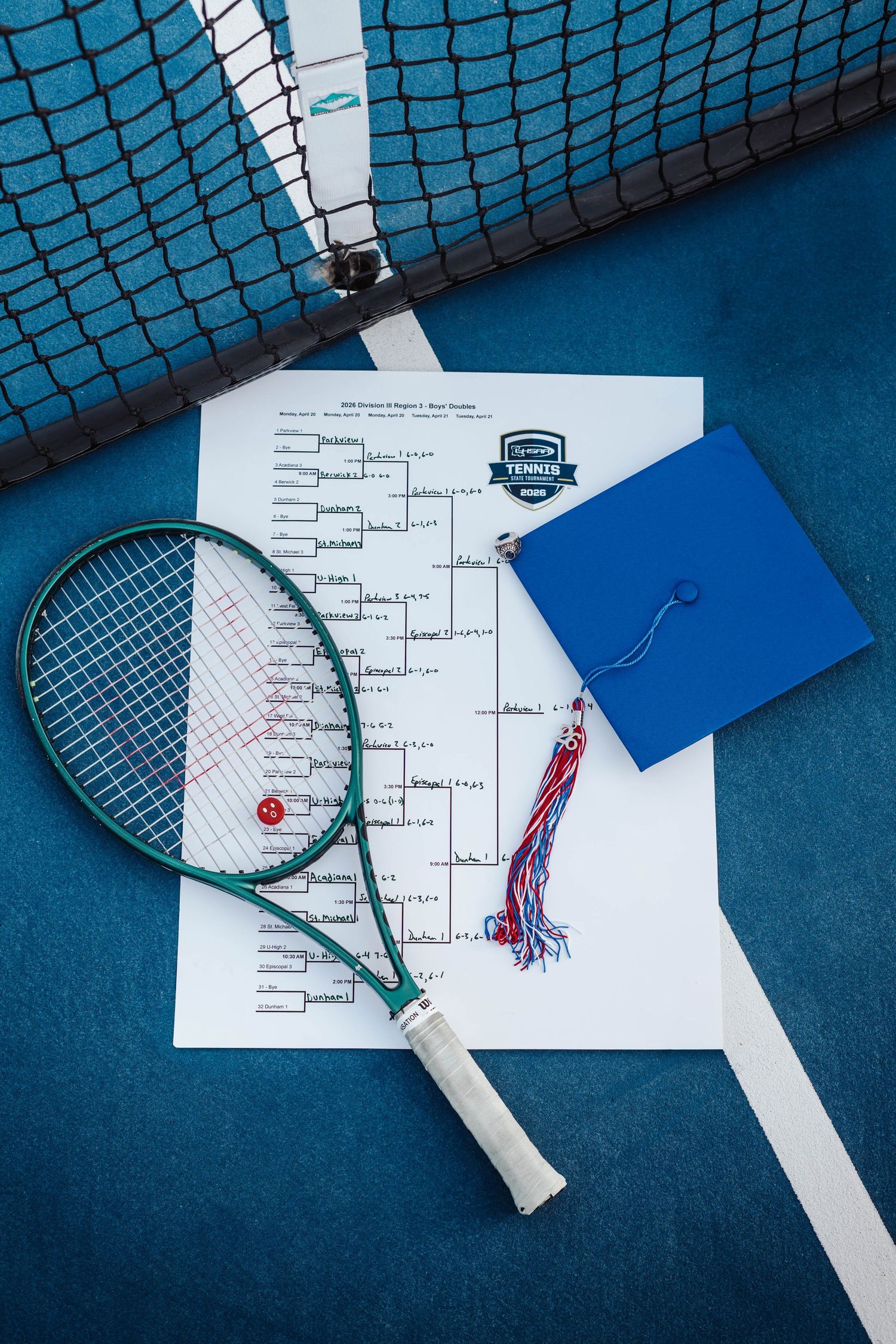 Tennis racket and graduation cap on a tournament bracket sheet on a blue court near the net.