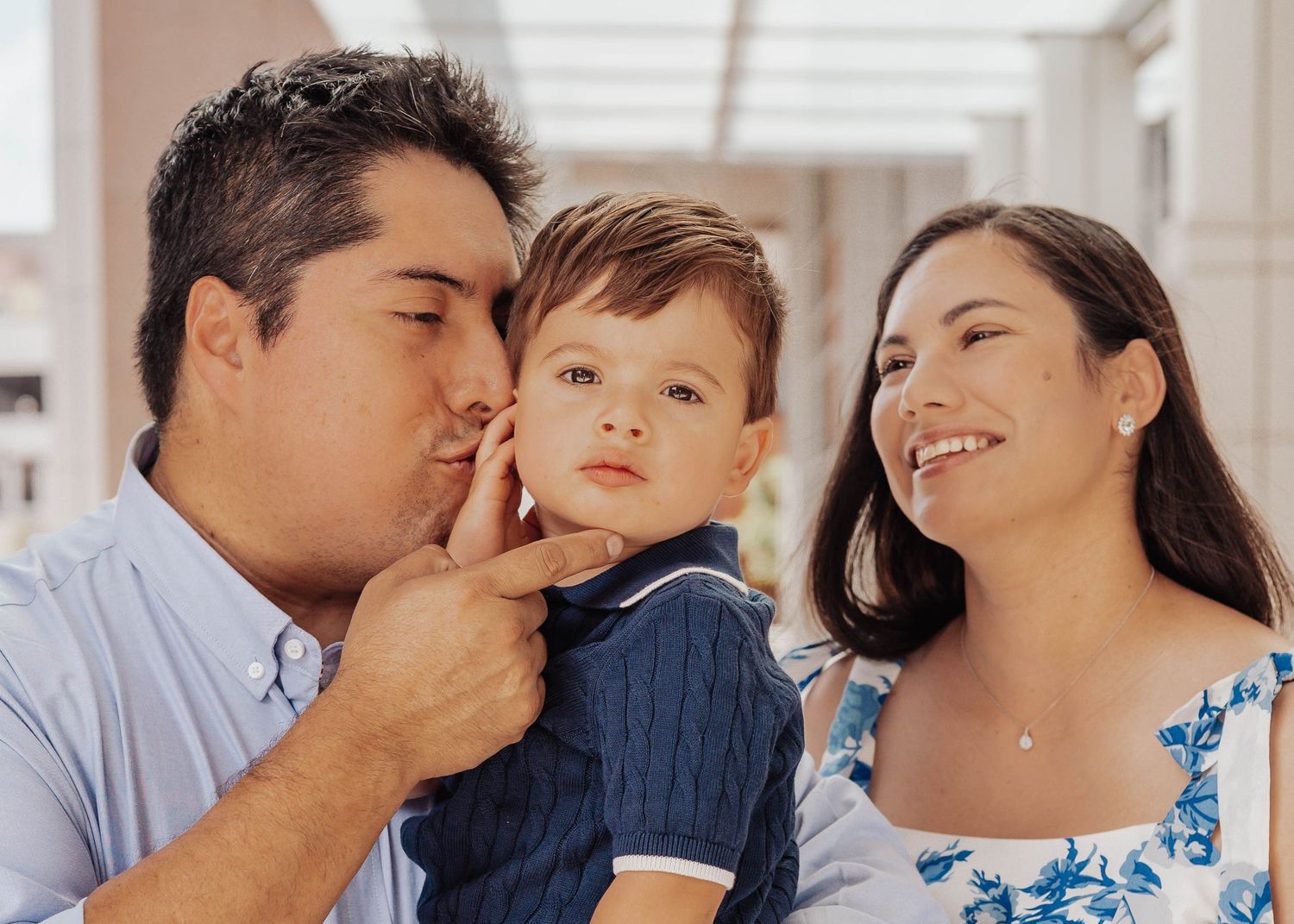 A loving family portrait with a father kissing his toddler son's cheek while the smiling mother holds the child.