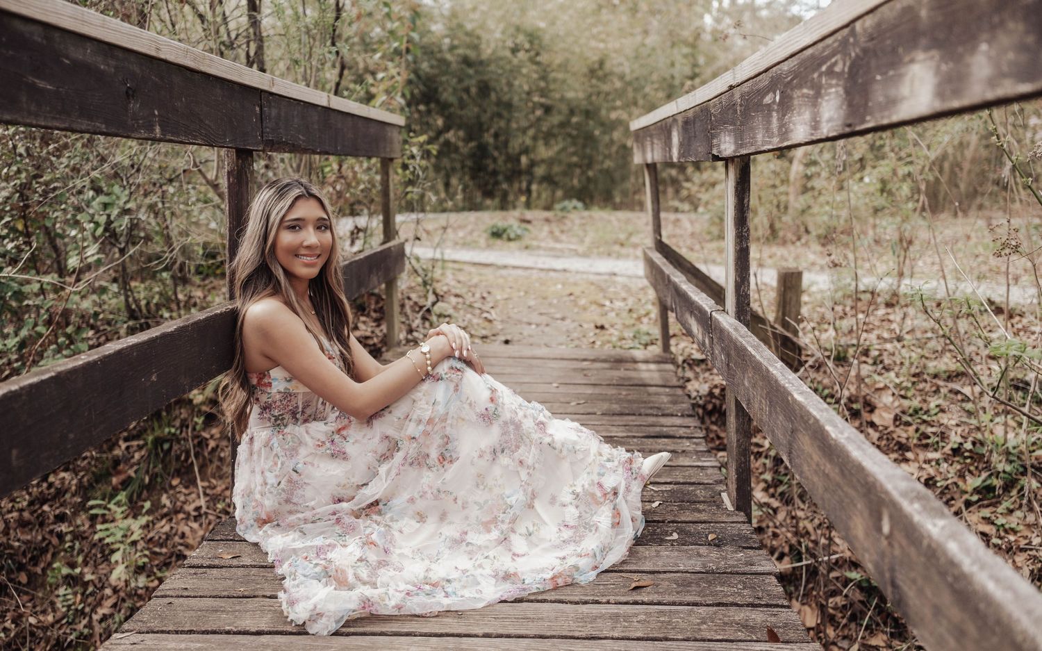 A flowing white wedding dress is showcased on a rustic wooden bridge surrounded by autumn foliage.