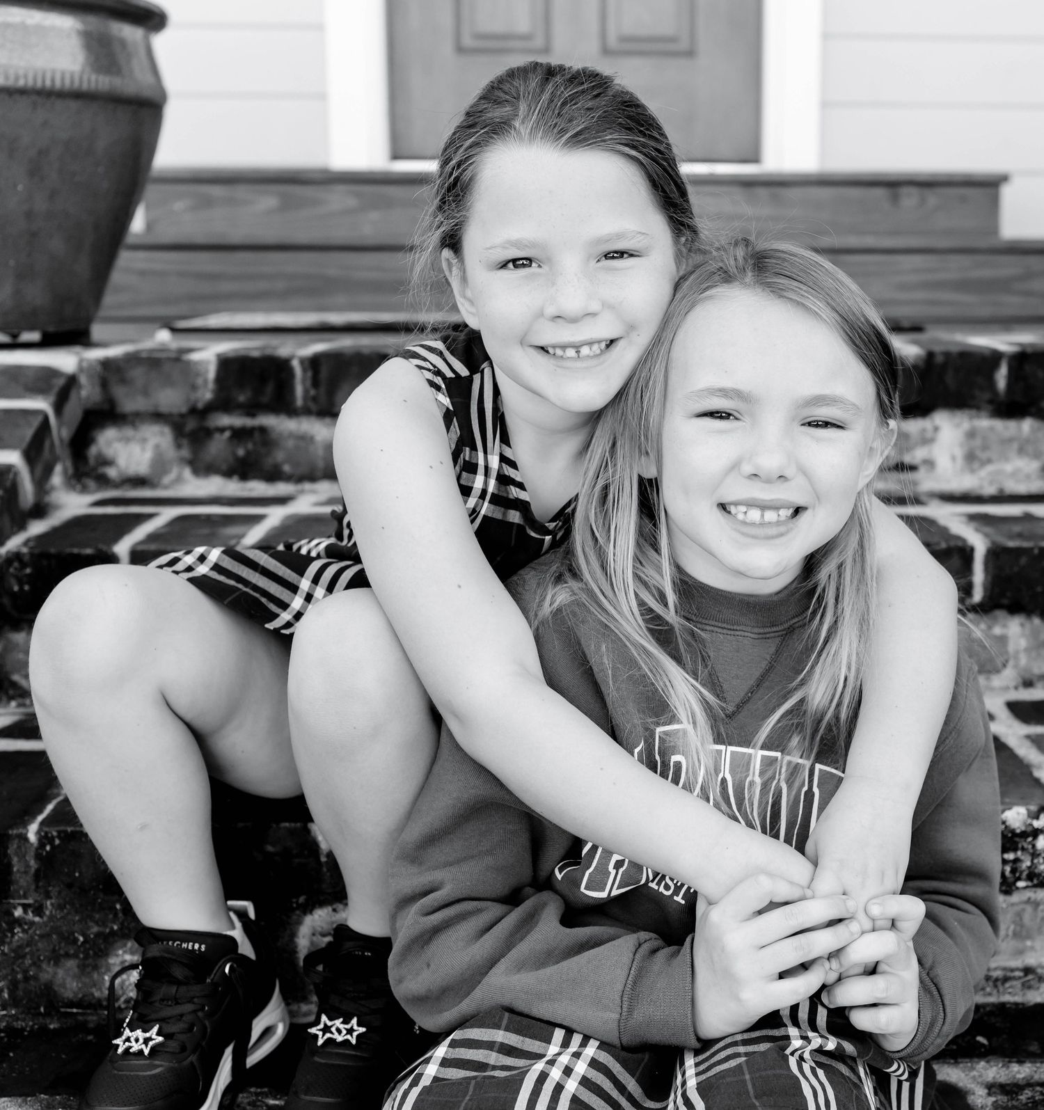 Back-to-school portraits in Baton Rouge — two sisters holding each other on the front porch, capturing authentic, timeless childhood moments