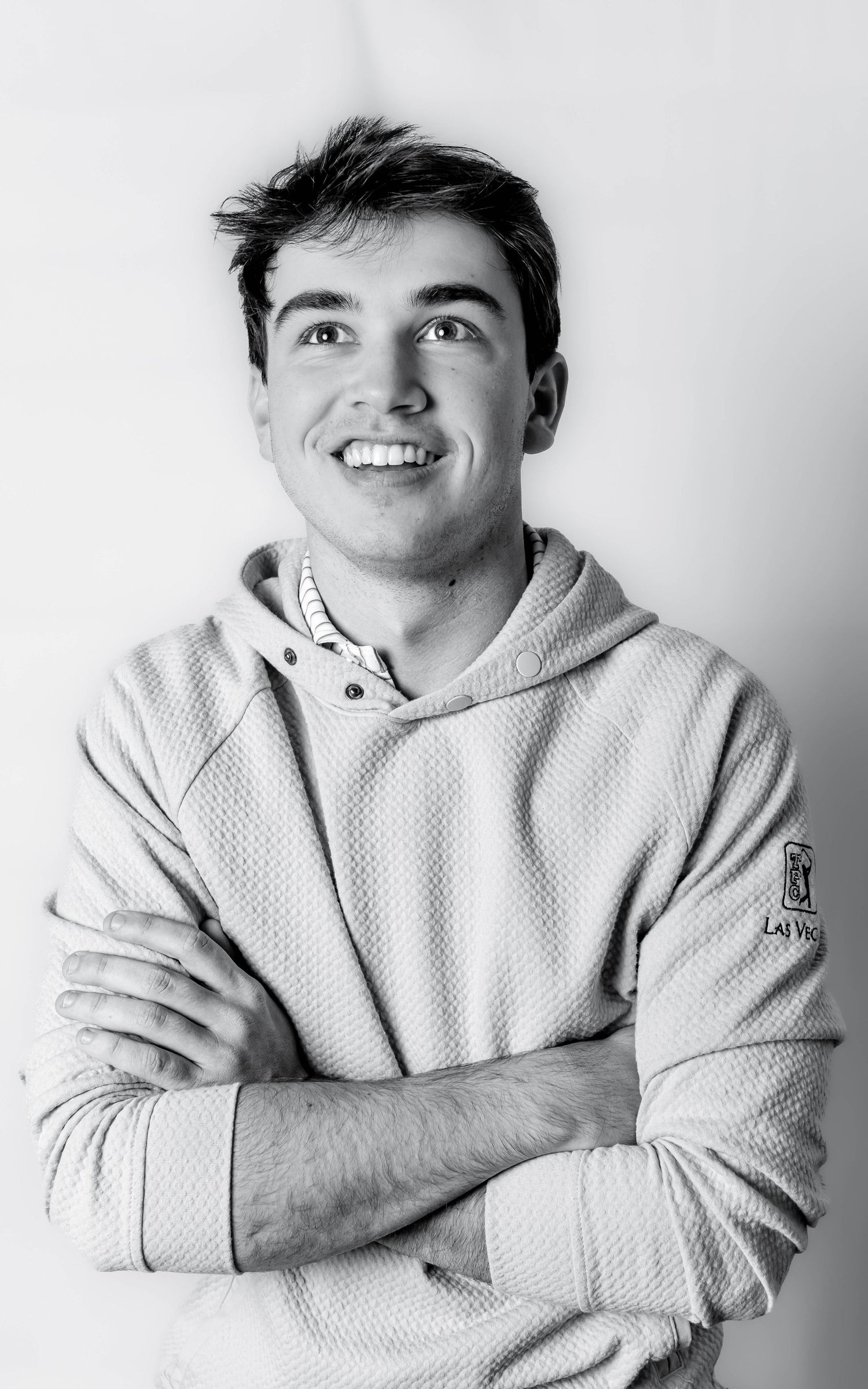 Smiling young man with arms crossed wearing a textured hoodie, black and white portrait photo.