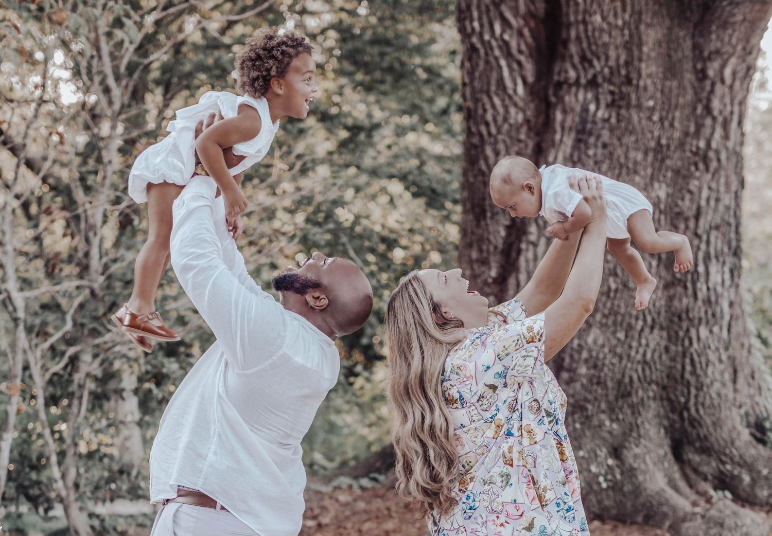A couple in white outfits dance together in a forest setting during a romantic outdoor photoshoot.
