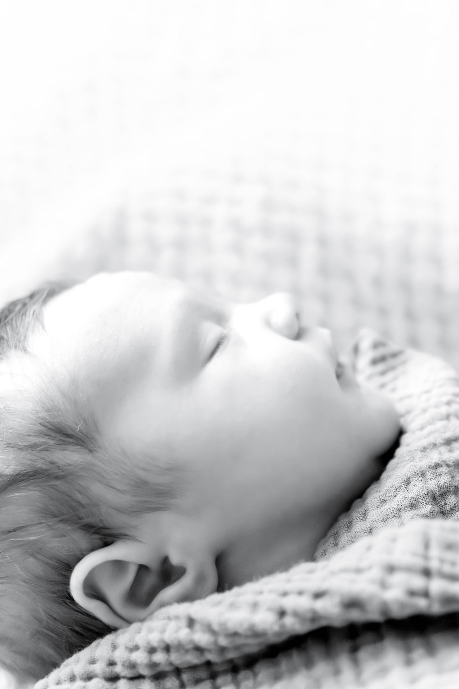 Black and white close-up of a peaceful sleeping newborn baby wrapped in a soft textured blanket.