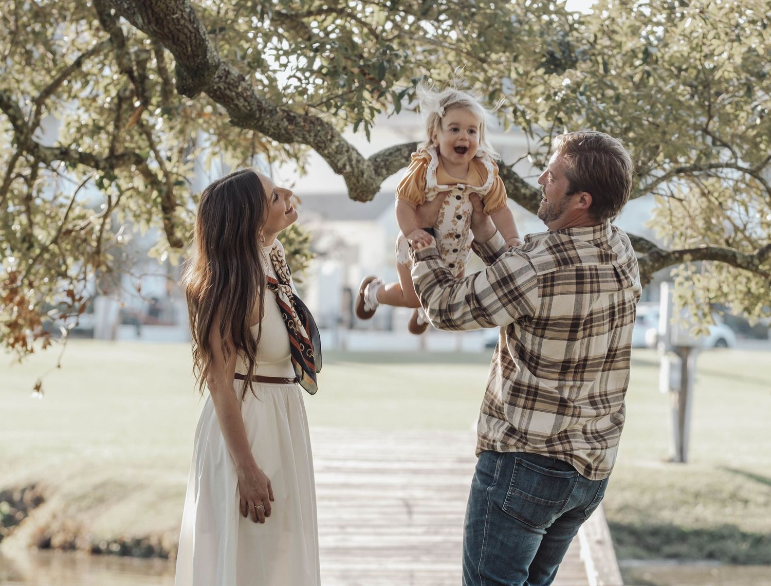 A loving family spends time together outdoors under a tree on a sunny afternoon.