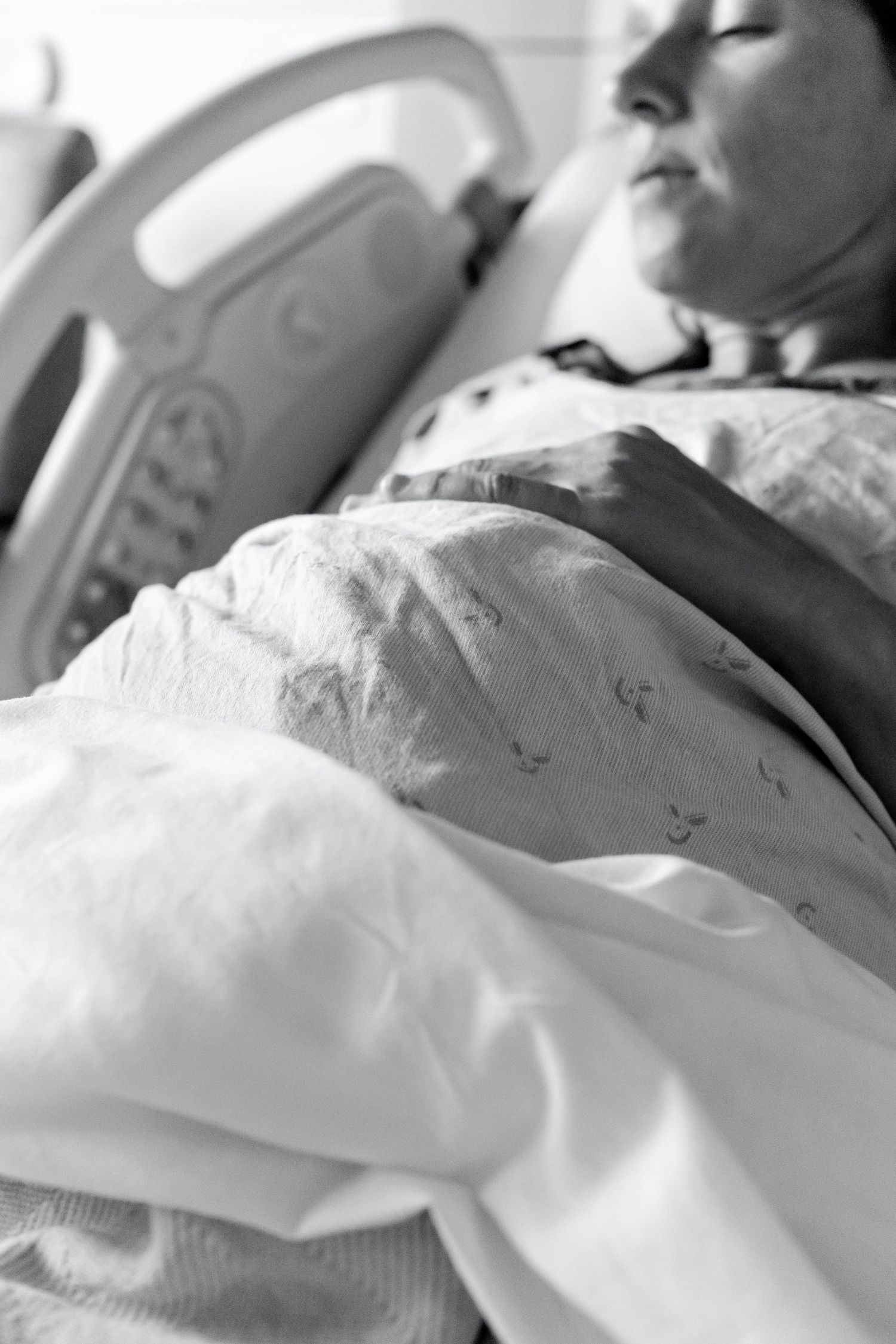 Black and white photo of a pregnant woman resting in a hospital bed wearing a patient gown.