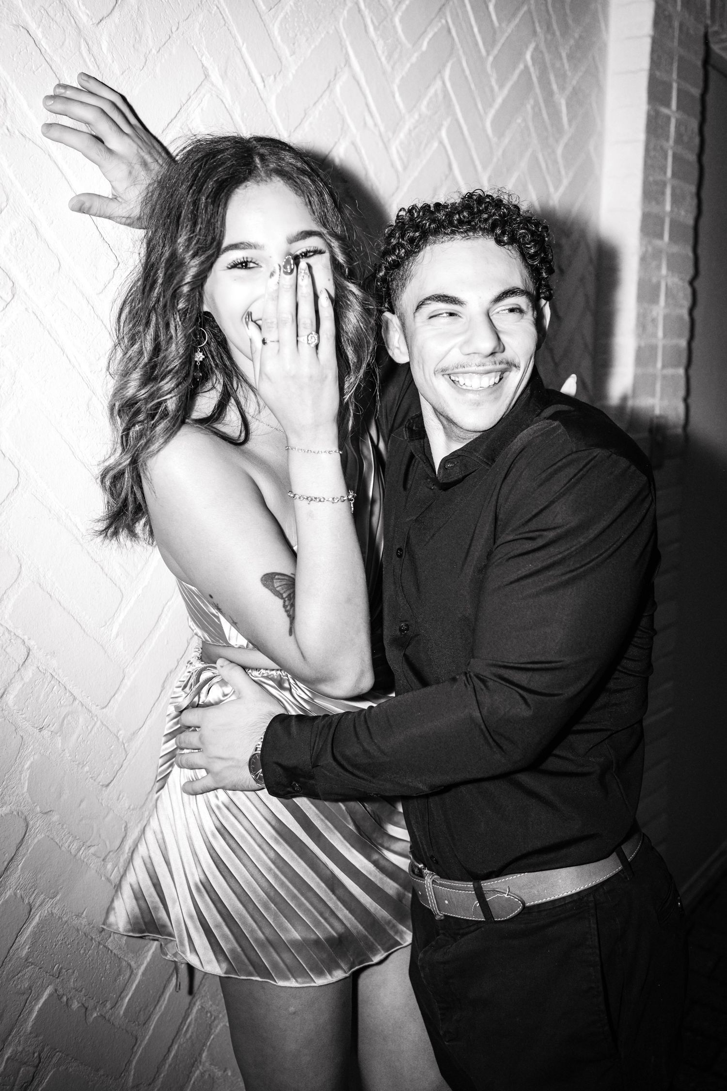 A black and white photo showing two people laughing and embracing against a textured wall.