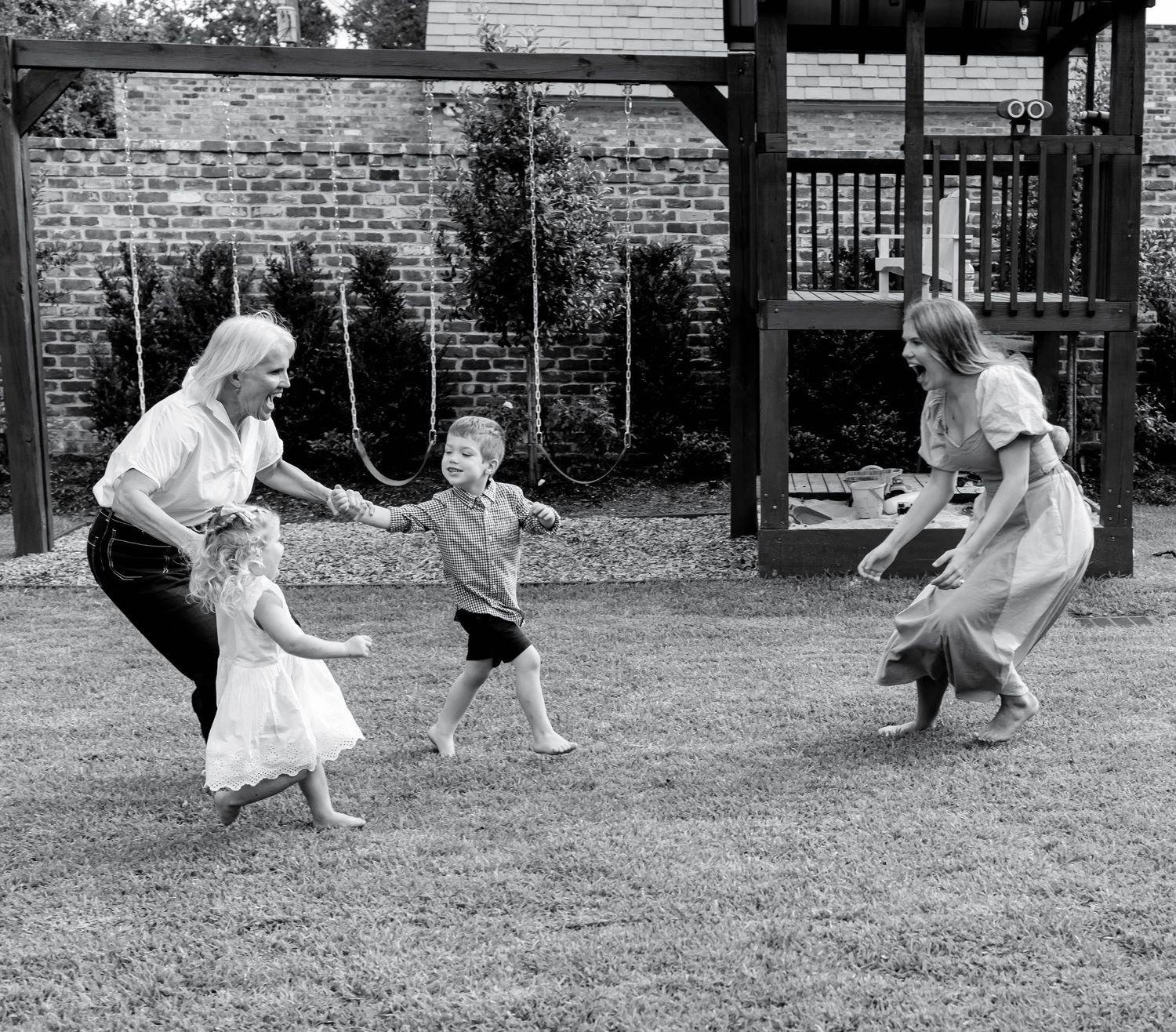 A vintage black and white photograph showing people playing together outdoors in a backyard with a brick wall backdrop.