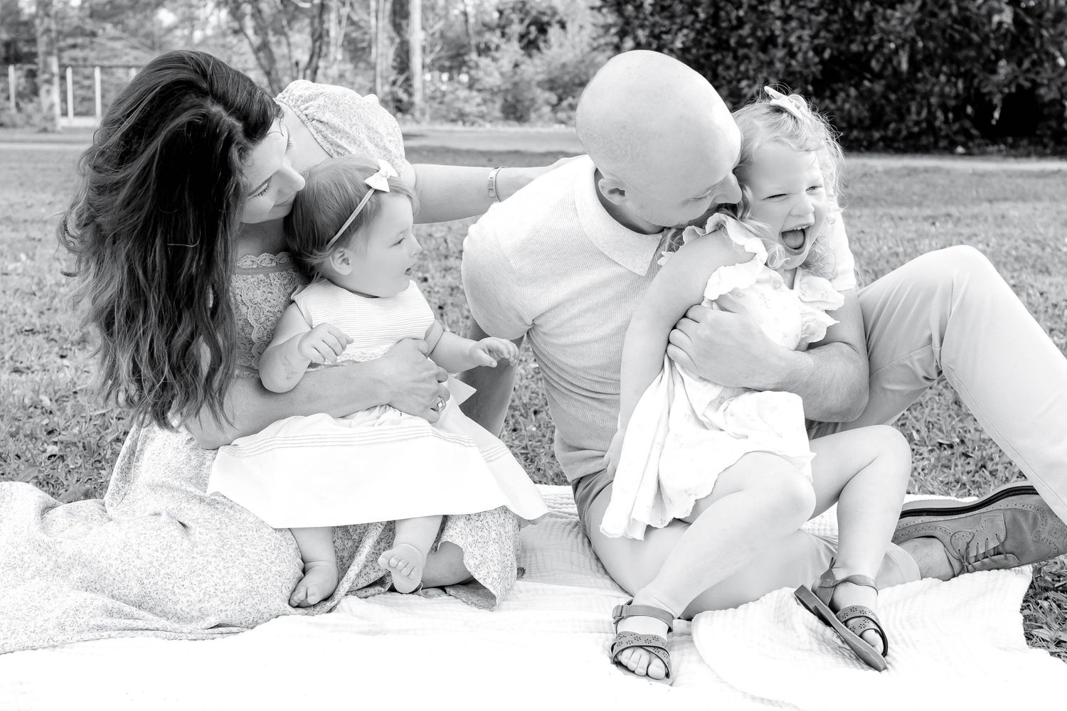 Black and white family photo of parents with two young children sitting on a blanket outdoors.