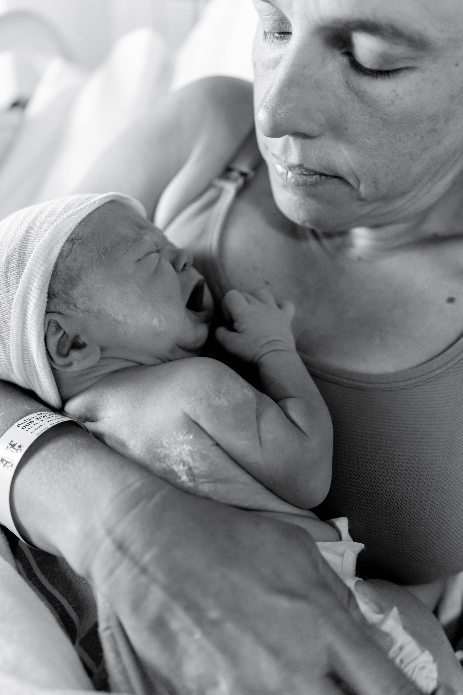 Black and white photo of a mother tenderly holding her newborn baby in a hospital room after birth.
