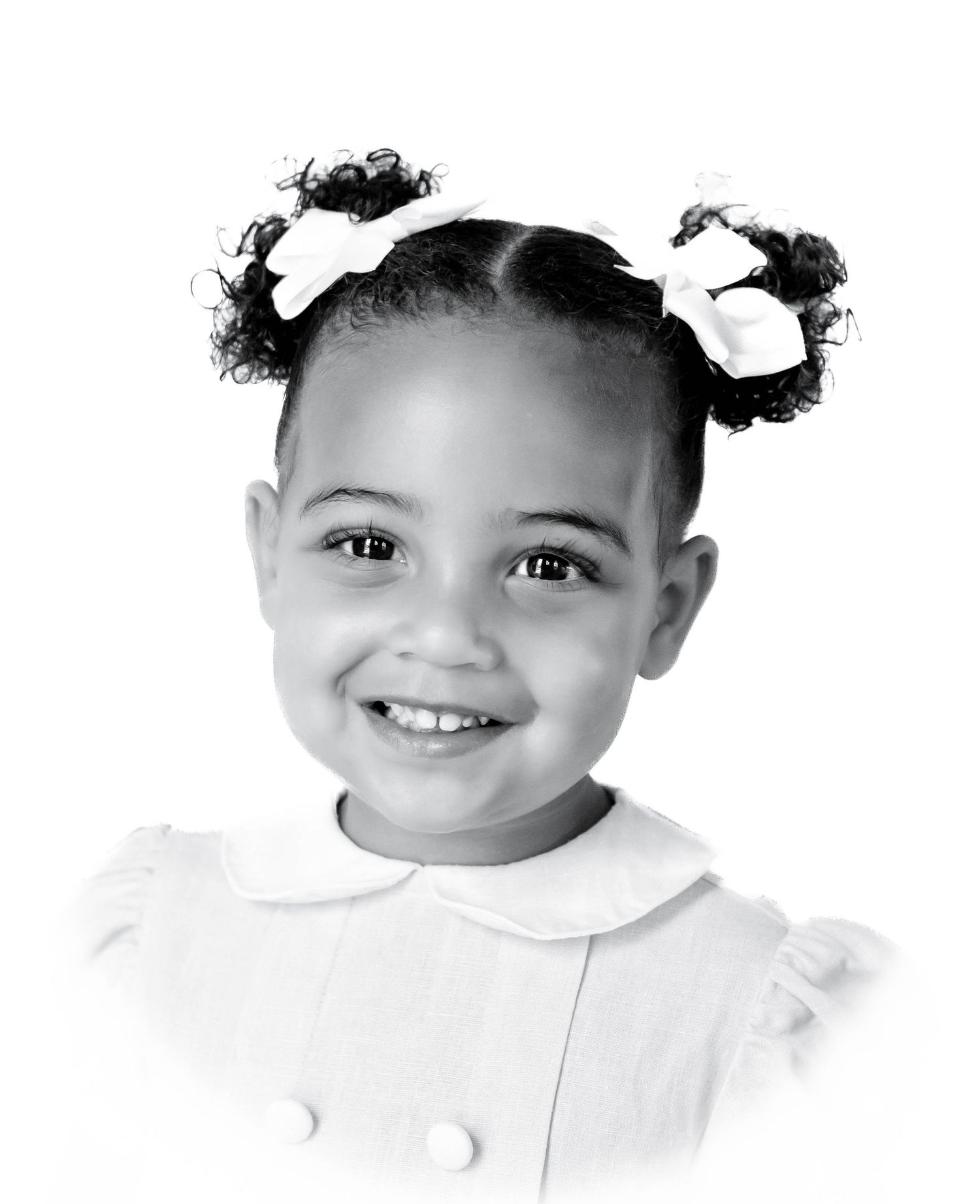 Black and white portrait of a young child with hair bows wearing a white collared dress with button details.