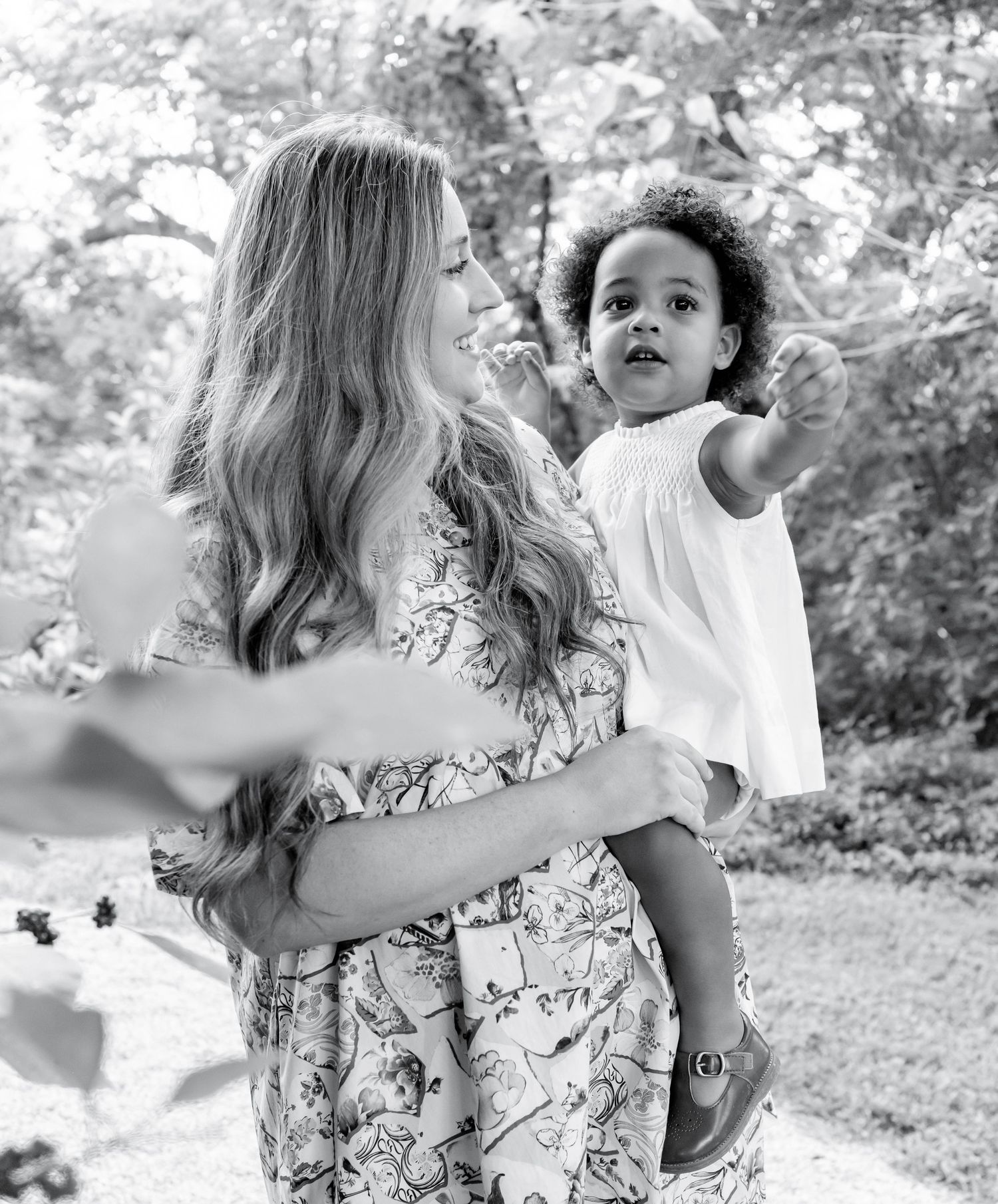 A candid black and white photo of a parent and child sharing a tender moment outdoors in a natural setting.