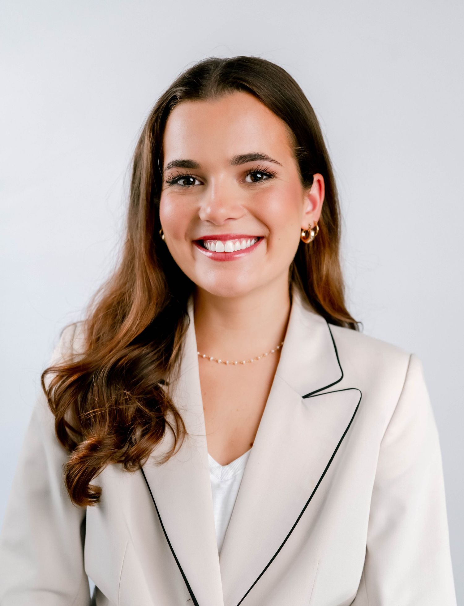 Professional wearing a white blazer with black trim smiles warmly against a light background.