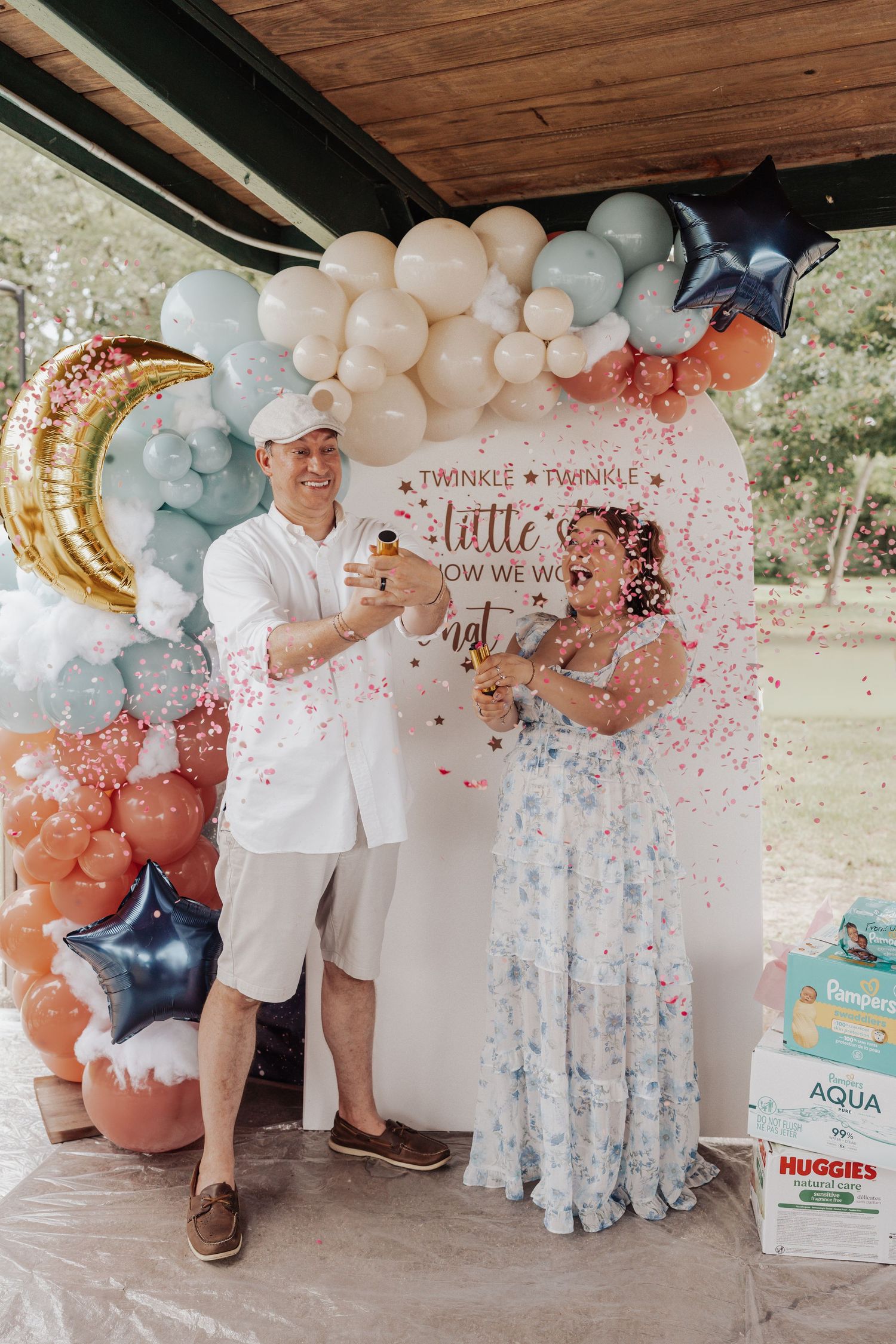 Couple celebrating a gender reveal party with confetti, balloons, and a Twinkle Twinkle backdrop outdoors.