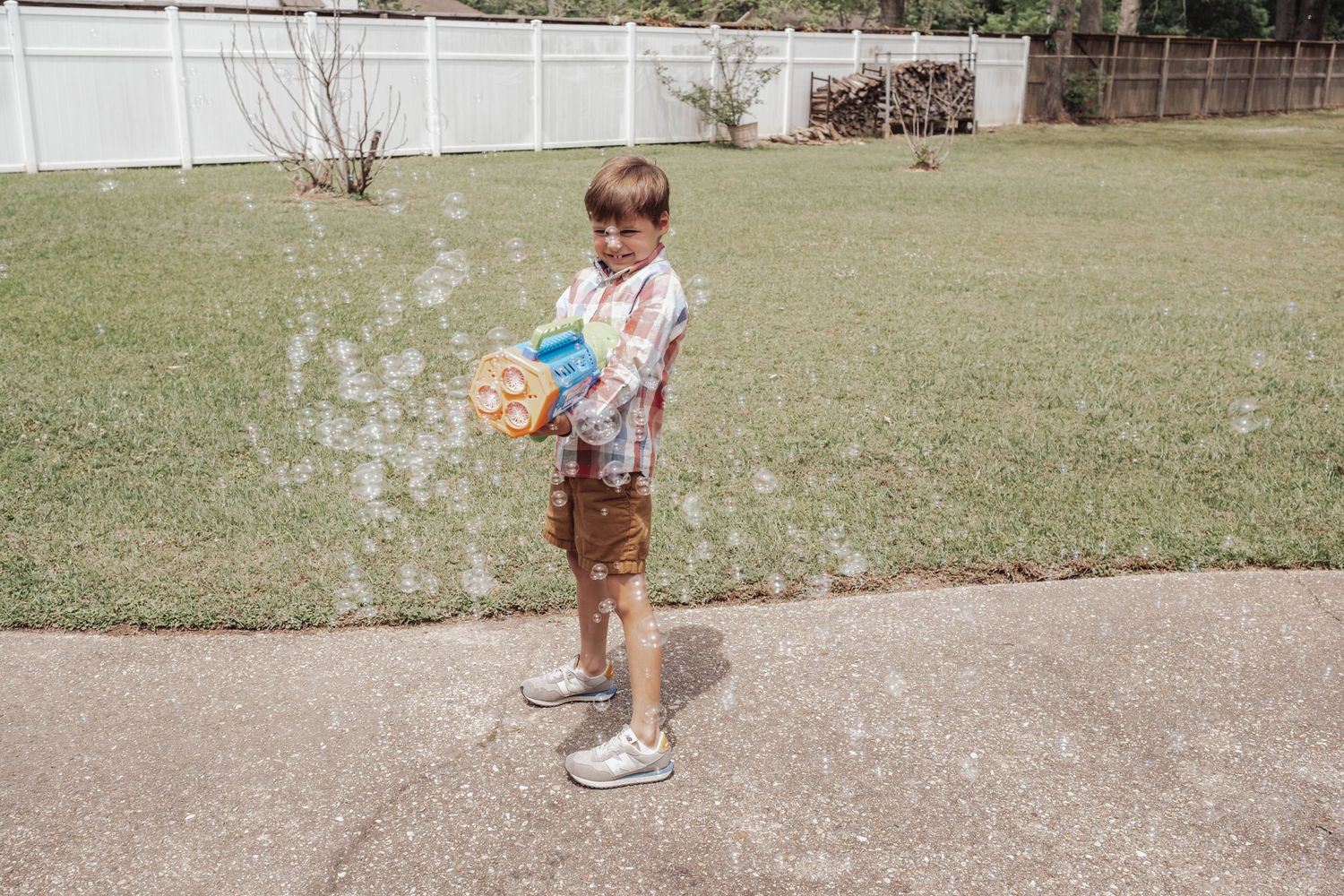 A young child in a floral dress and sneakers runs and plays on a paved pathway near a grassy lawn.