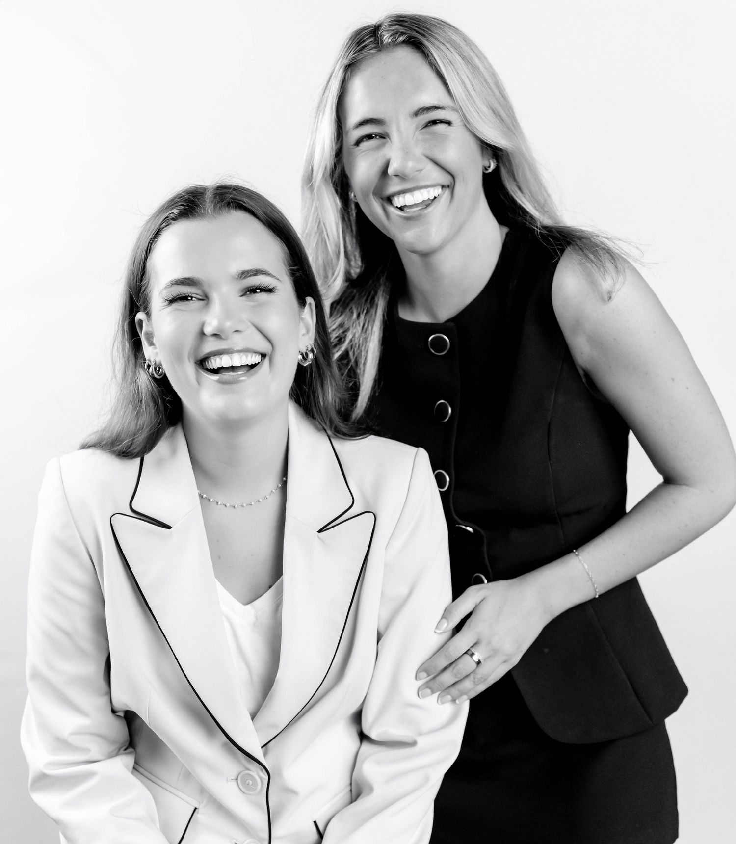 Two people in black and white attire share genuine laughter during a professional photoshoot.
