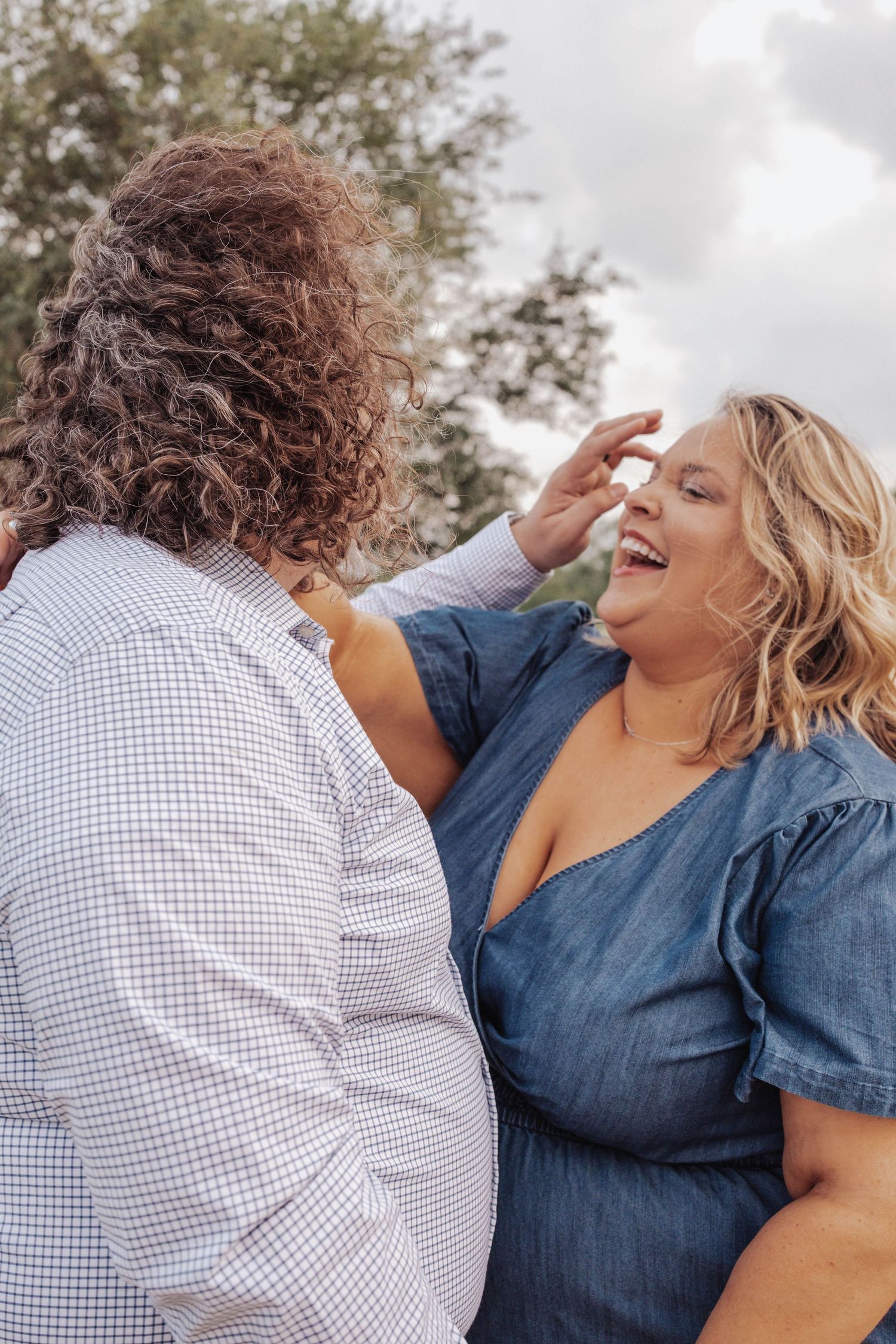 Couple in denim and checkered shirts sharing candid laughter during outdoor photo session.