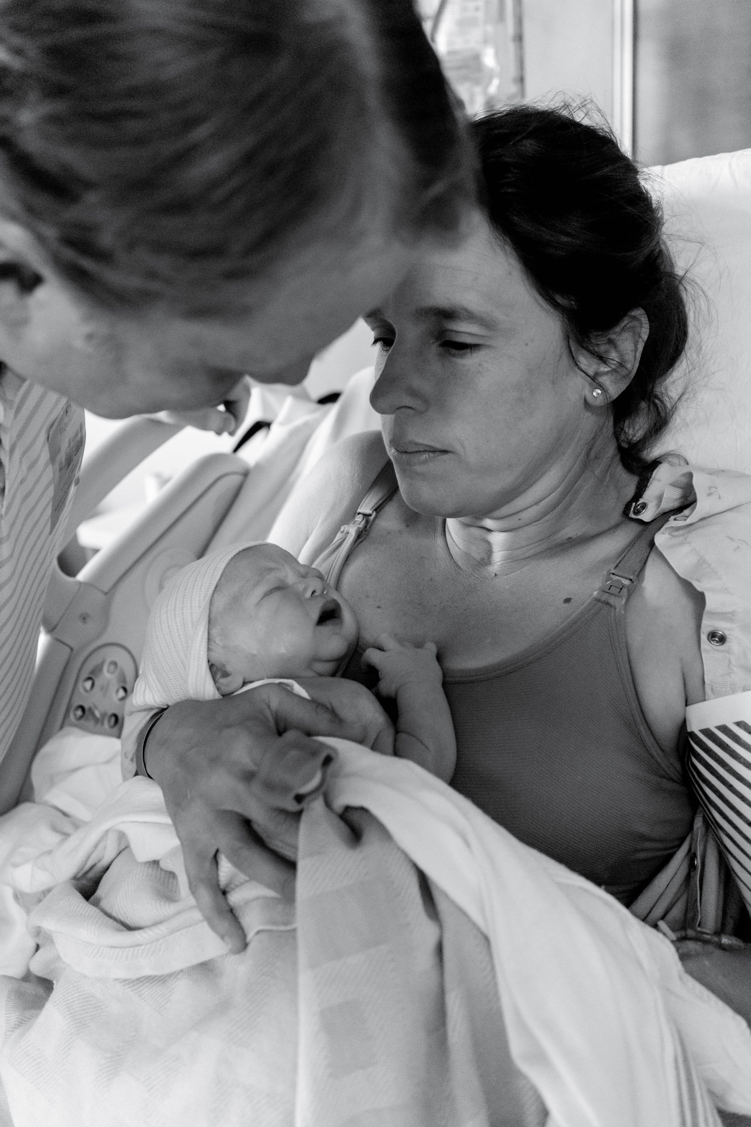 Black and white photo of new parents tenderly gazing at their newborn baby in a hospital room.