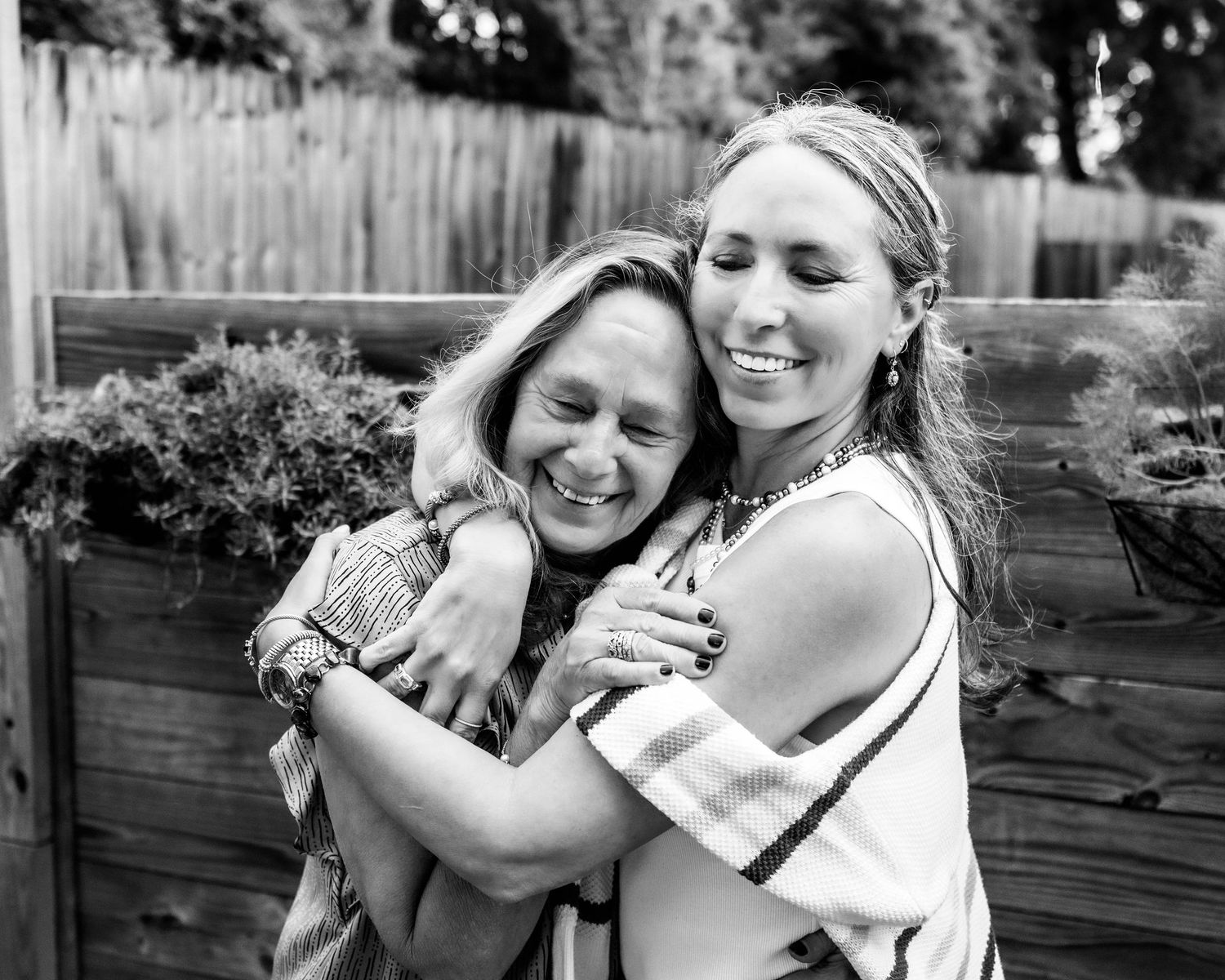 A candid black and white moment of shared joy and laughter in a backyard garden setting.