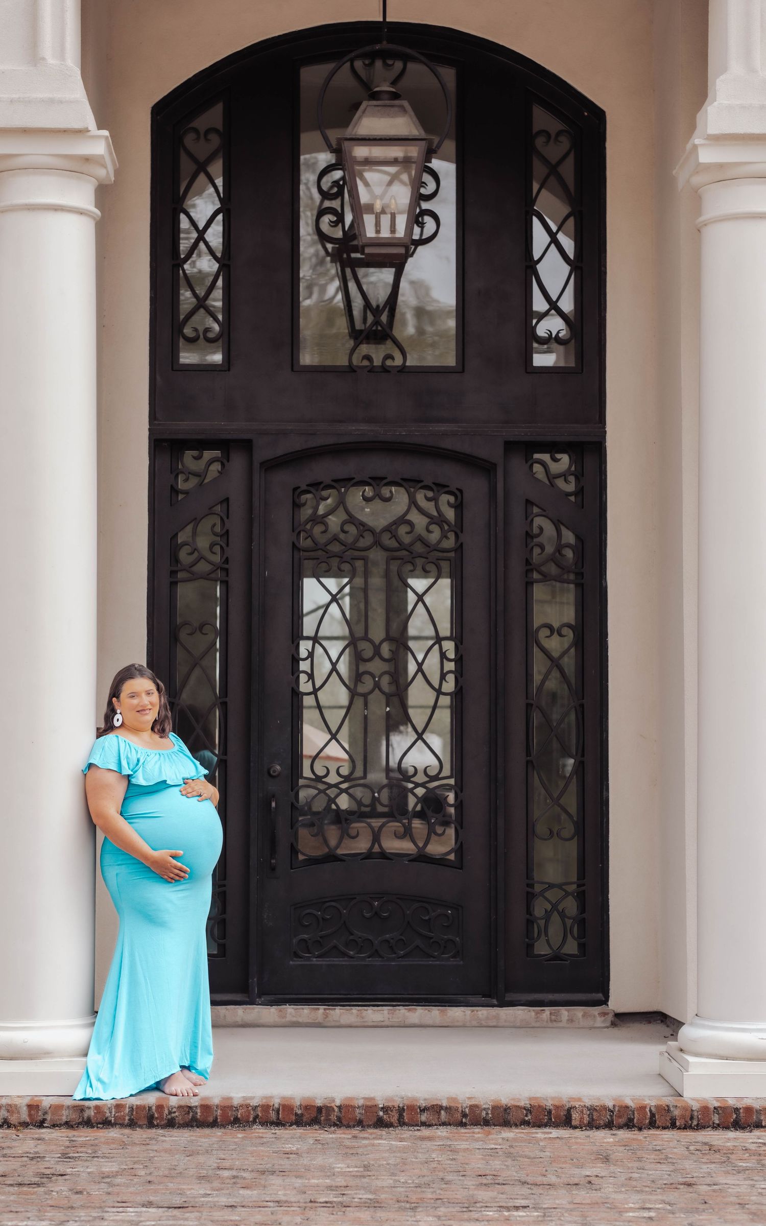 A person in a turquoise dress stands in front of an elegant black iron door with decorative glass panels.