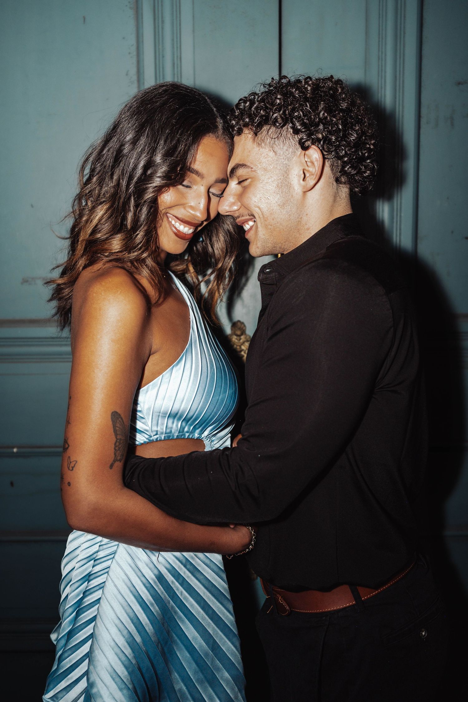 A joyful couple embraces and laughs together, woman in blue striped dress and man in black shirt.