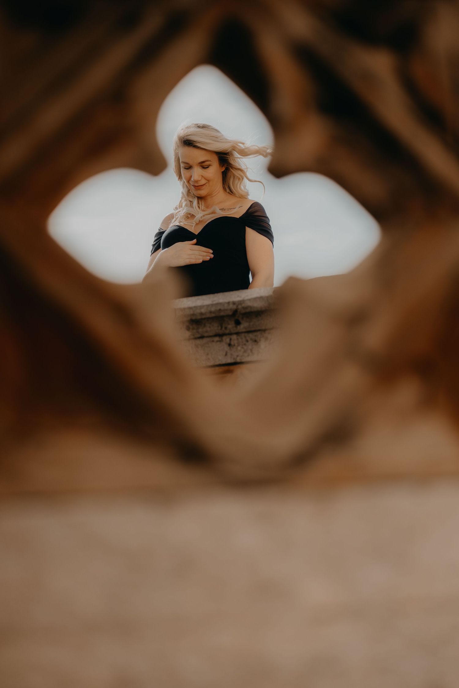 Maternity photo of a figure in black dress viewed through architectural detail.