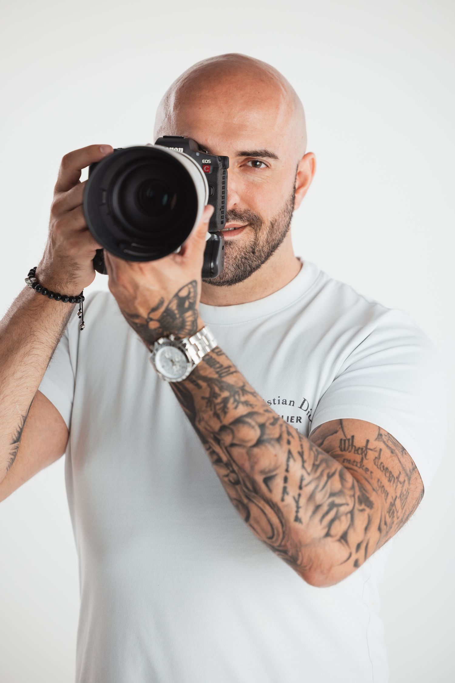 Professional photographer with tattooed arm holding DSLR camera against white background.